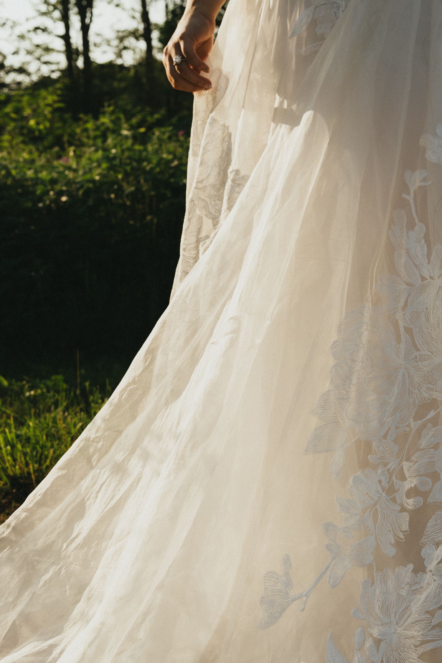 Close-up of elegant lace wedding dress train glowing in golden sunlight outdoors.