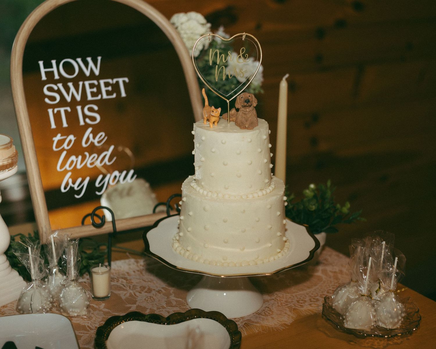 Three-tier white wedding cake with heart topper displayed beside sign reading How Sweet It Is To Be Loved By You.