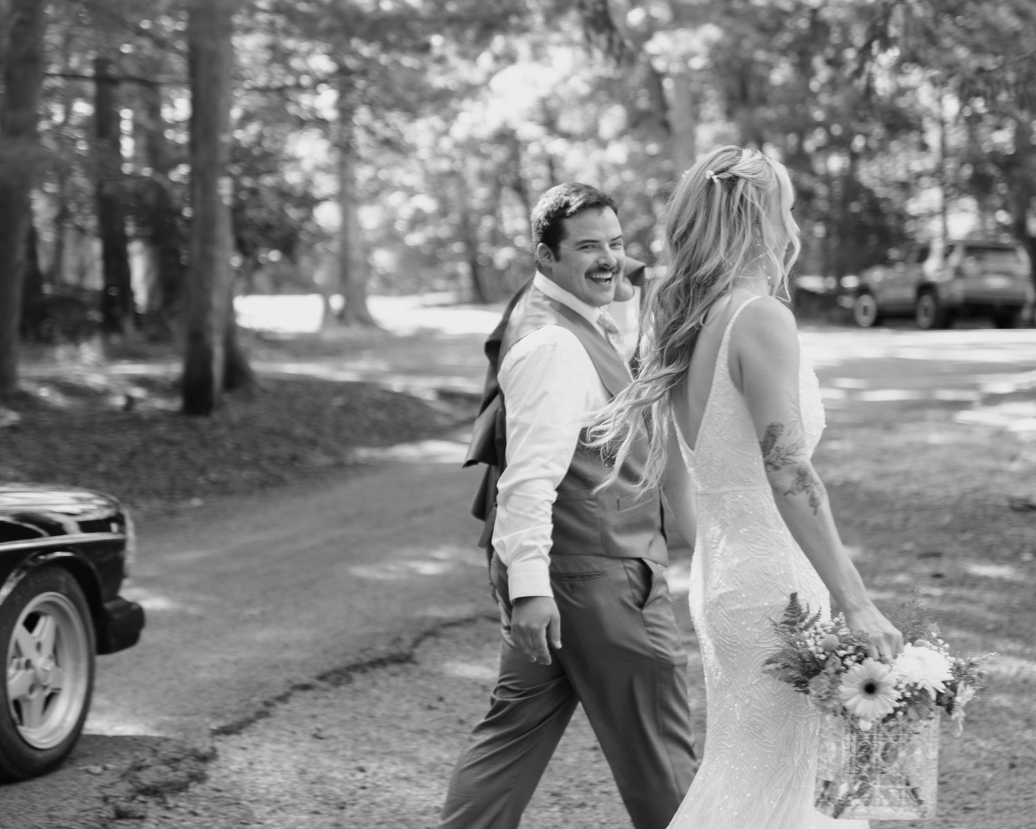 Black and white photo of smiling bride and groom walking together outdoors at a woodland wedding venue.