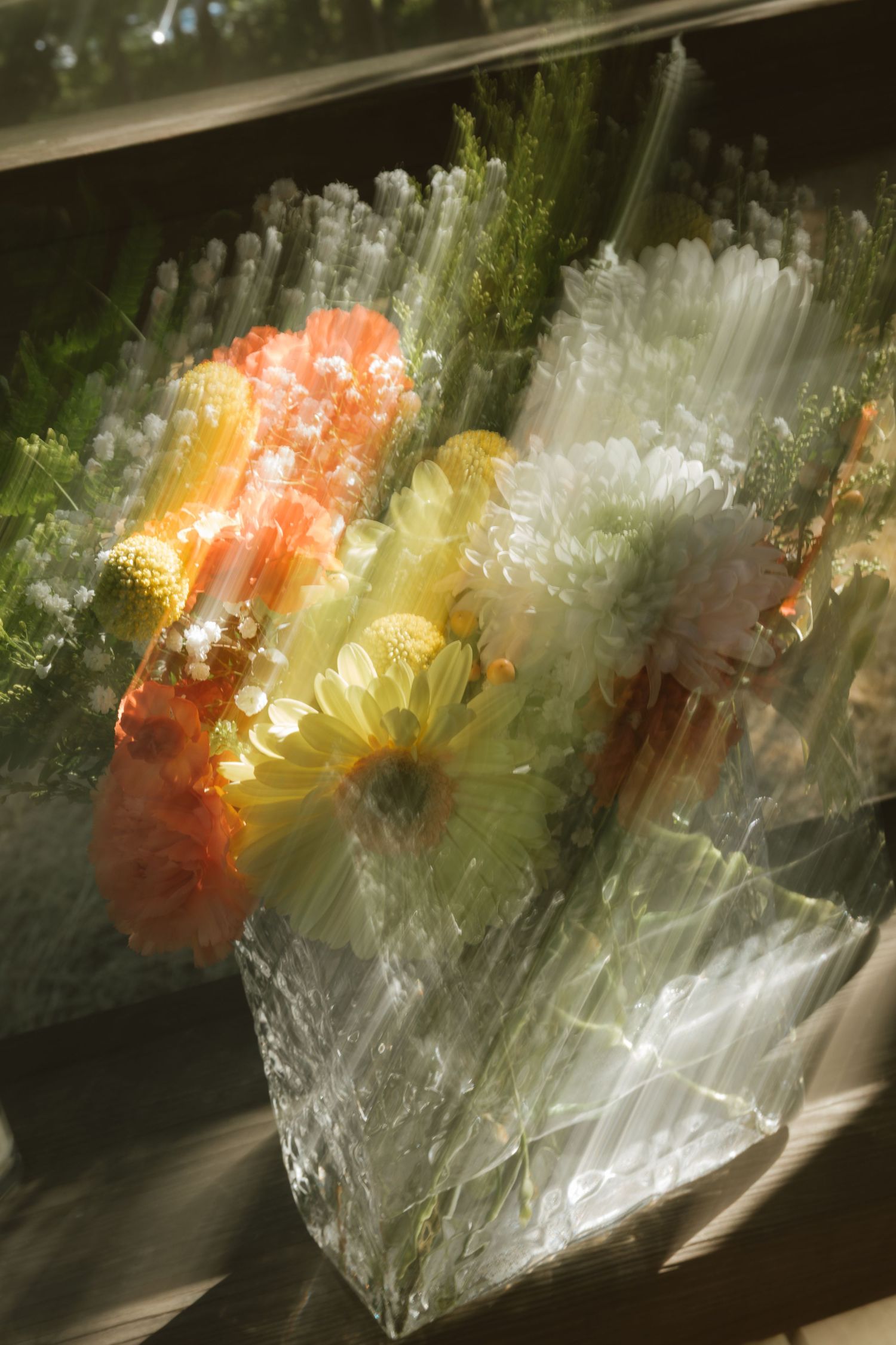 Crystal vase with colorful orange, yellow, and white chrysanthemums displayed in sunlight through a window.