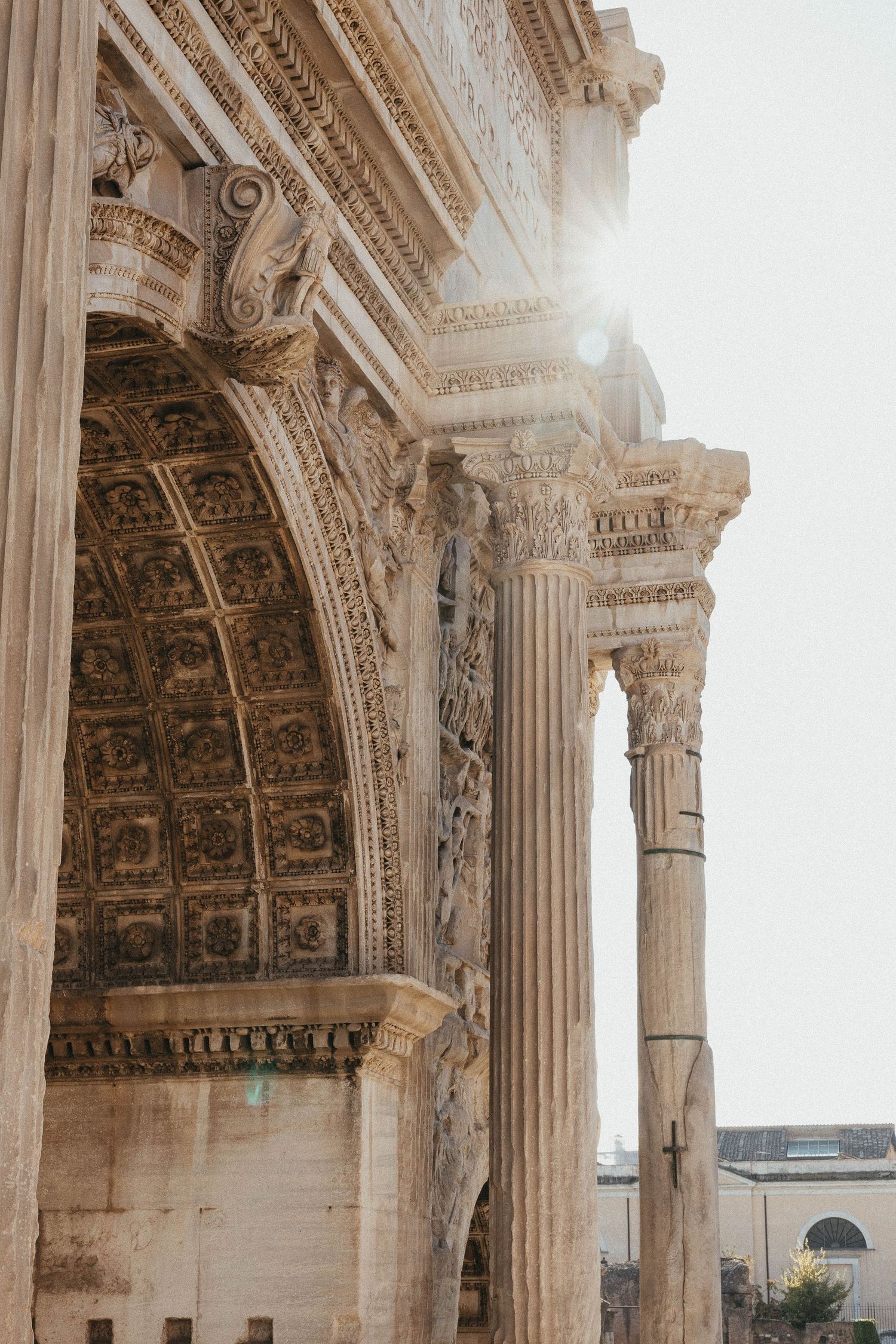 Ornate ancient Roman arch with intricate carvings and Corinthian columns bathed in sunlight.