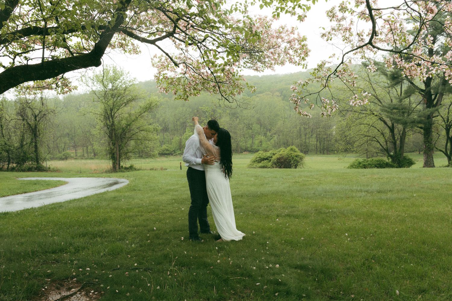 A couple dancing  in a lush green field during a light spring rain in The Poconos, perfect for adventurous elopement photography.