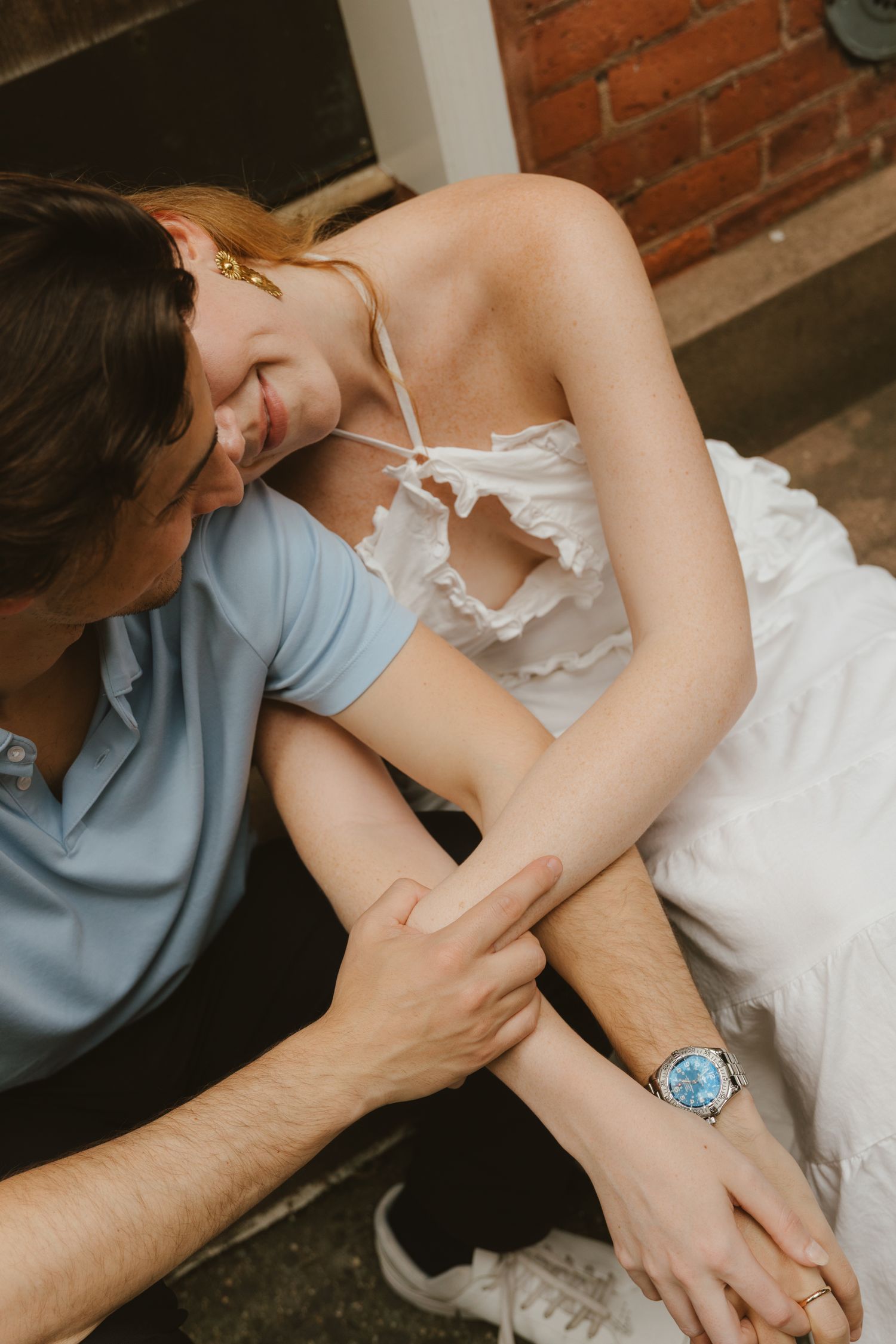 Couple sitting closely together, woman in white dress laughing as man whispers to her.