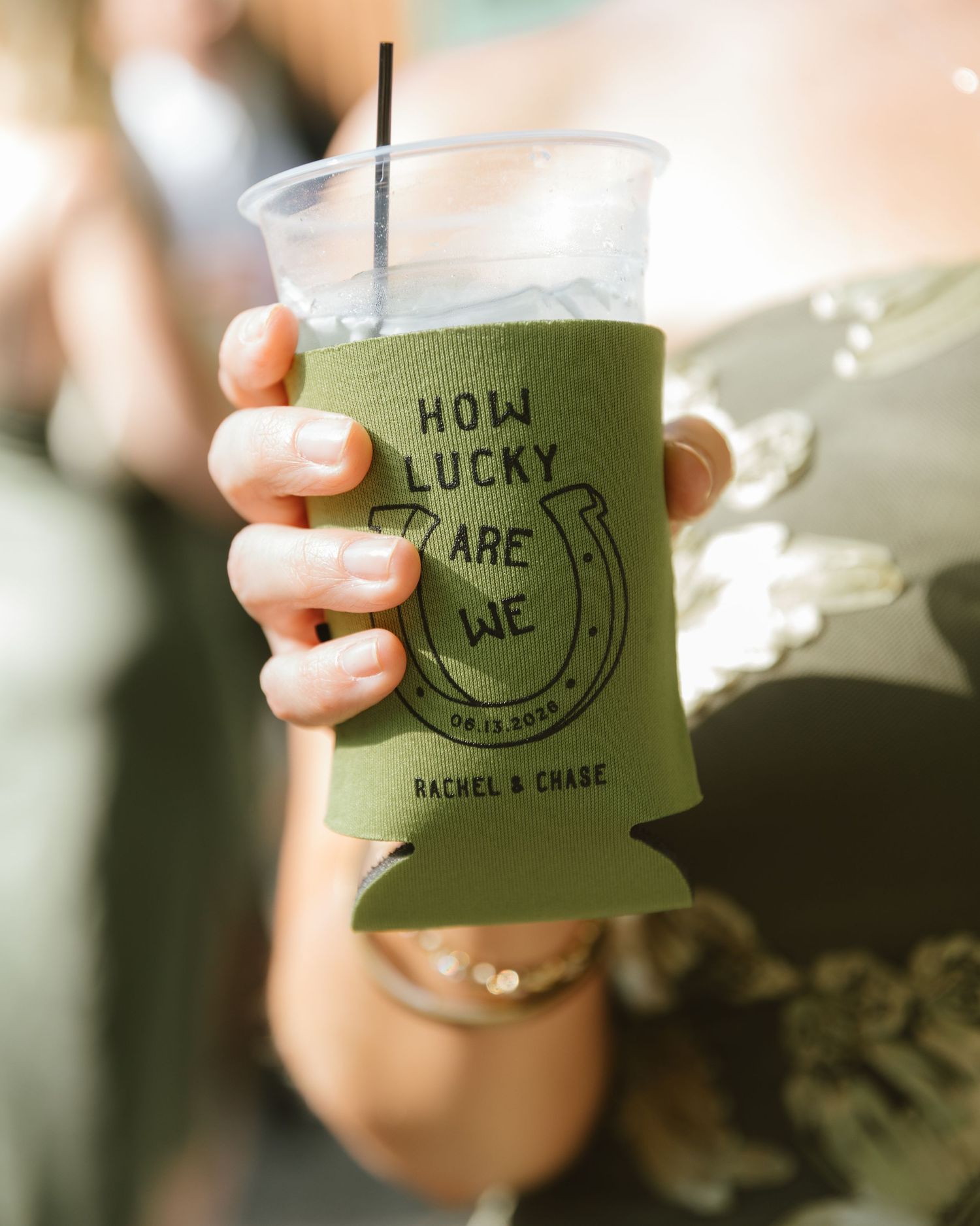 Hand holding a custom green koozie reading How Lucky Are We with a horseshoe design for Rachel and Chase wedding.