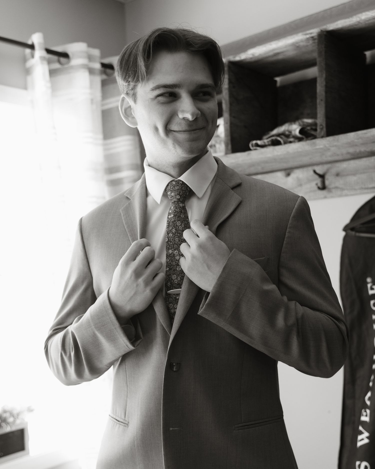 Young groom in gray suit adjusting tie in black and white getting ready photo.