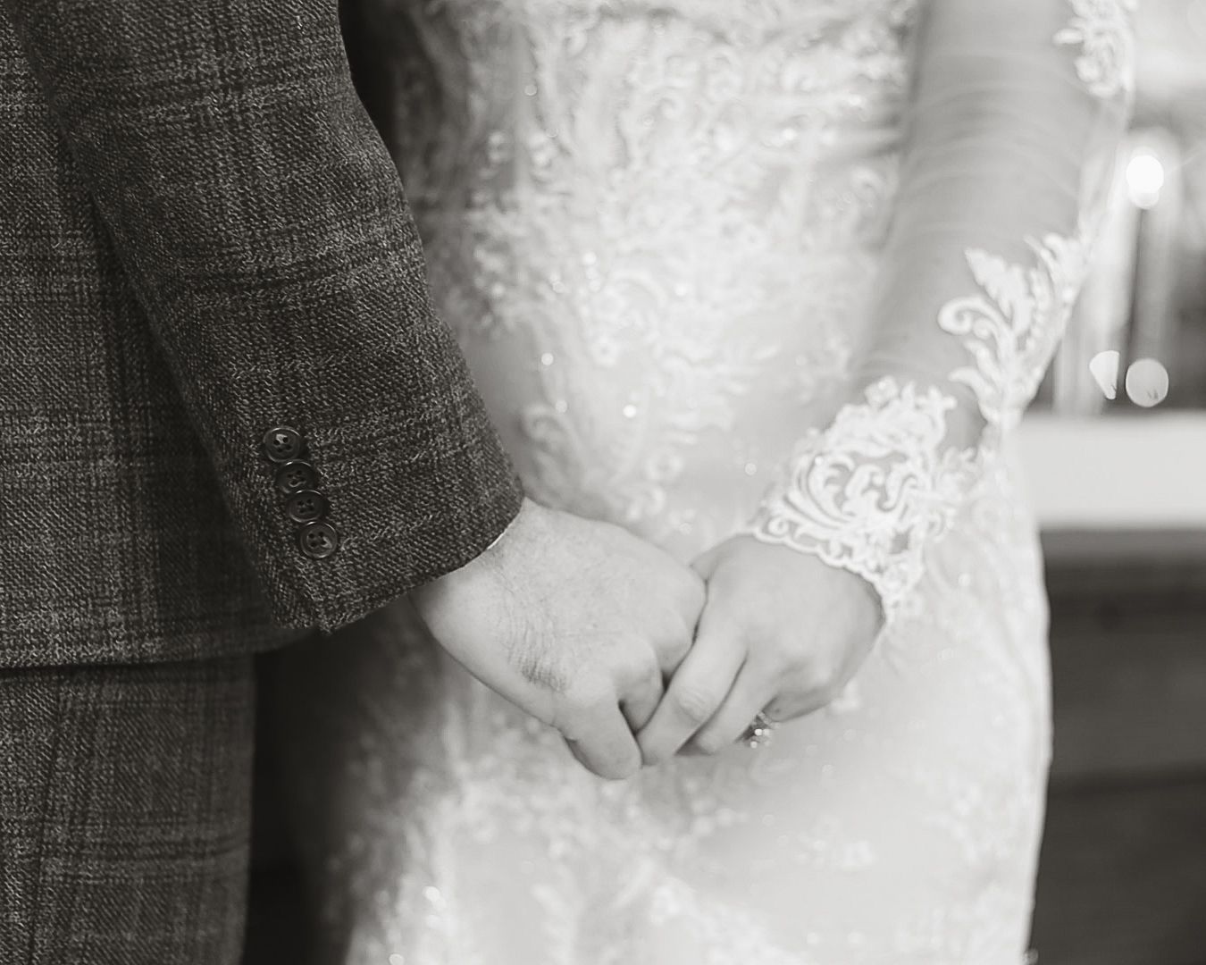 Black and white close-up of bride and groom holding hands in wedding attire.