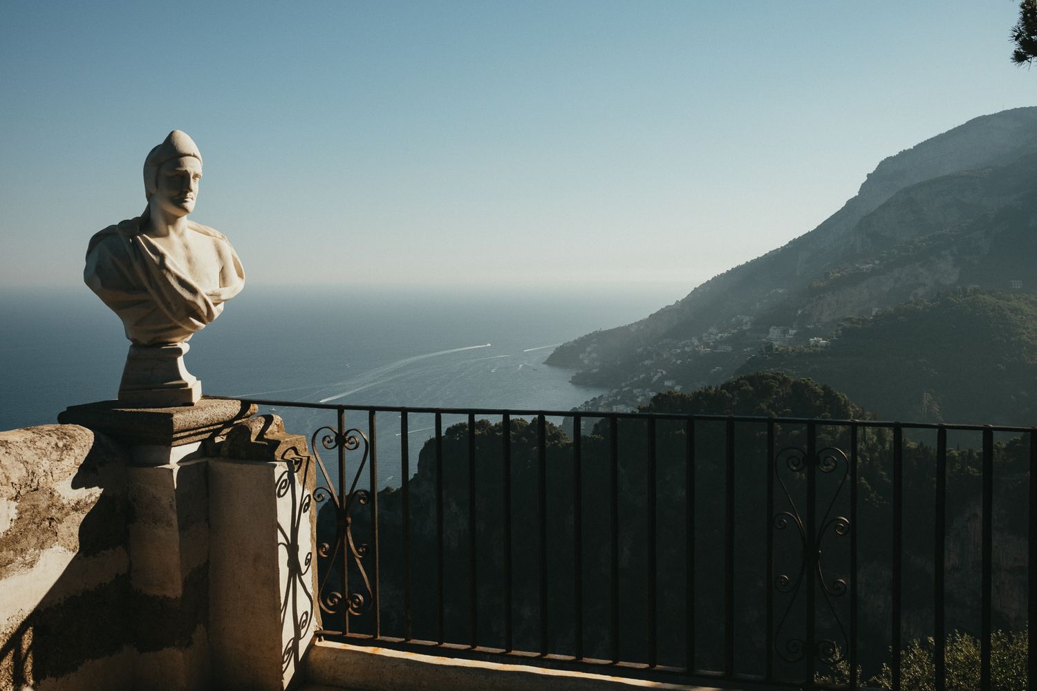 Stone bust sculpture on terrace overlooking stunning Amalfi Coast coastline and mountains.