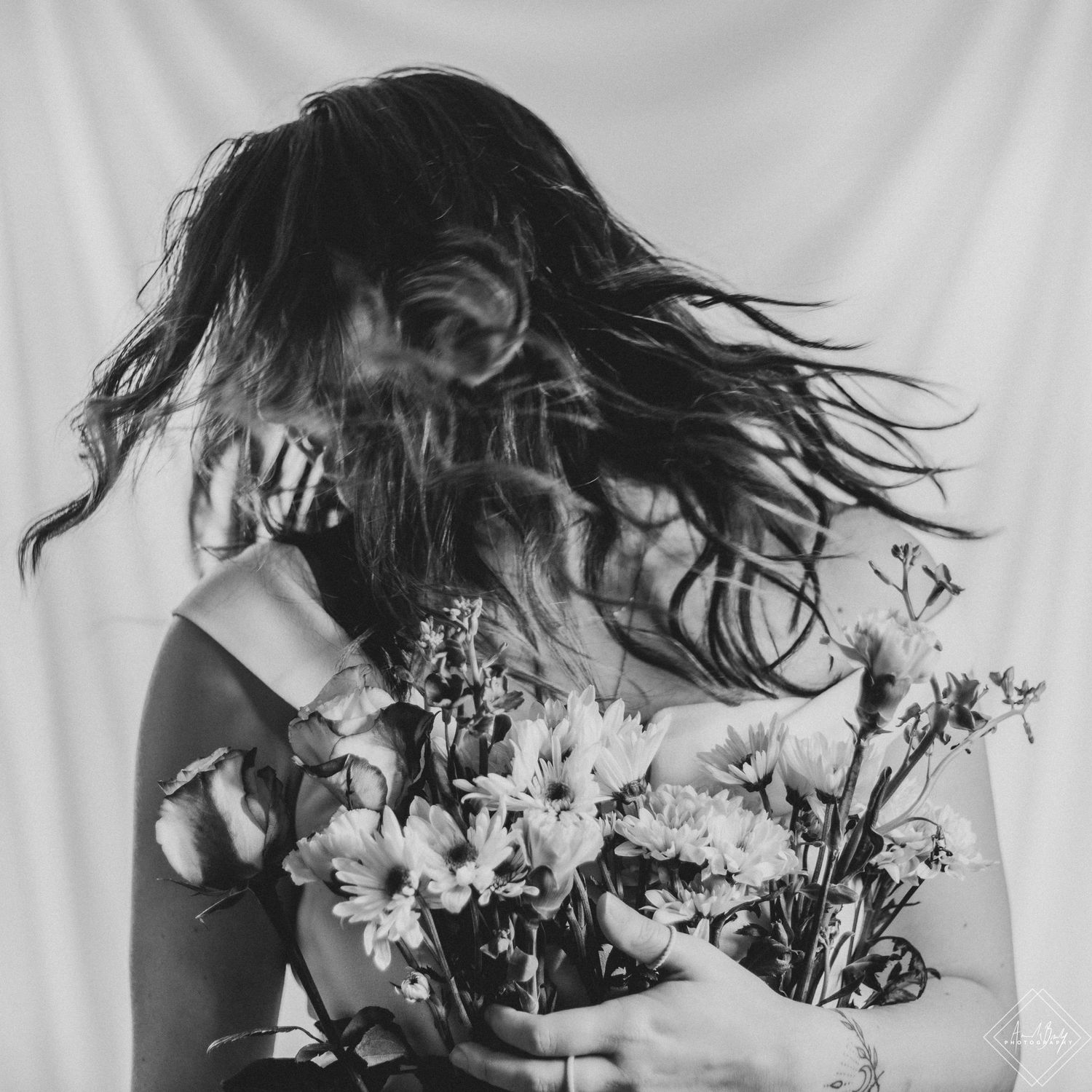 Black and white artistic photo of woman tossing hair holding bouquet of flowers.