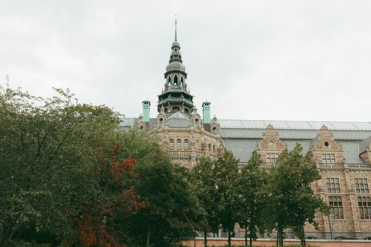 Historic Nordic Museum building with ornate spire surrounded by autumn trees in Stockholm.