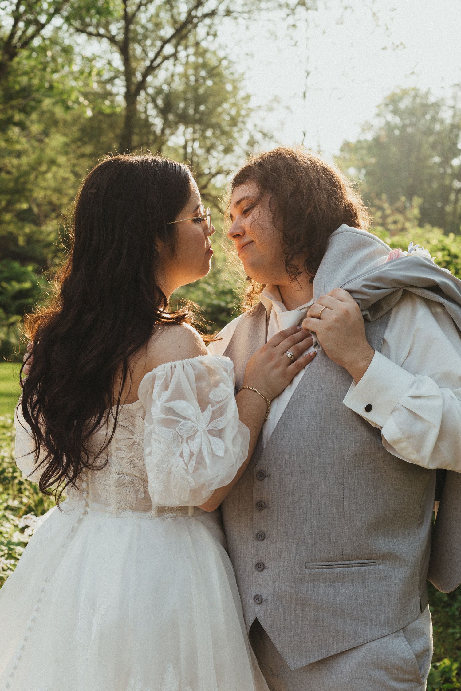 Bride and groom sharing a romantic moment in a sunlit garden, with bride in lace gown and groom in gray suit.
