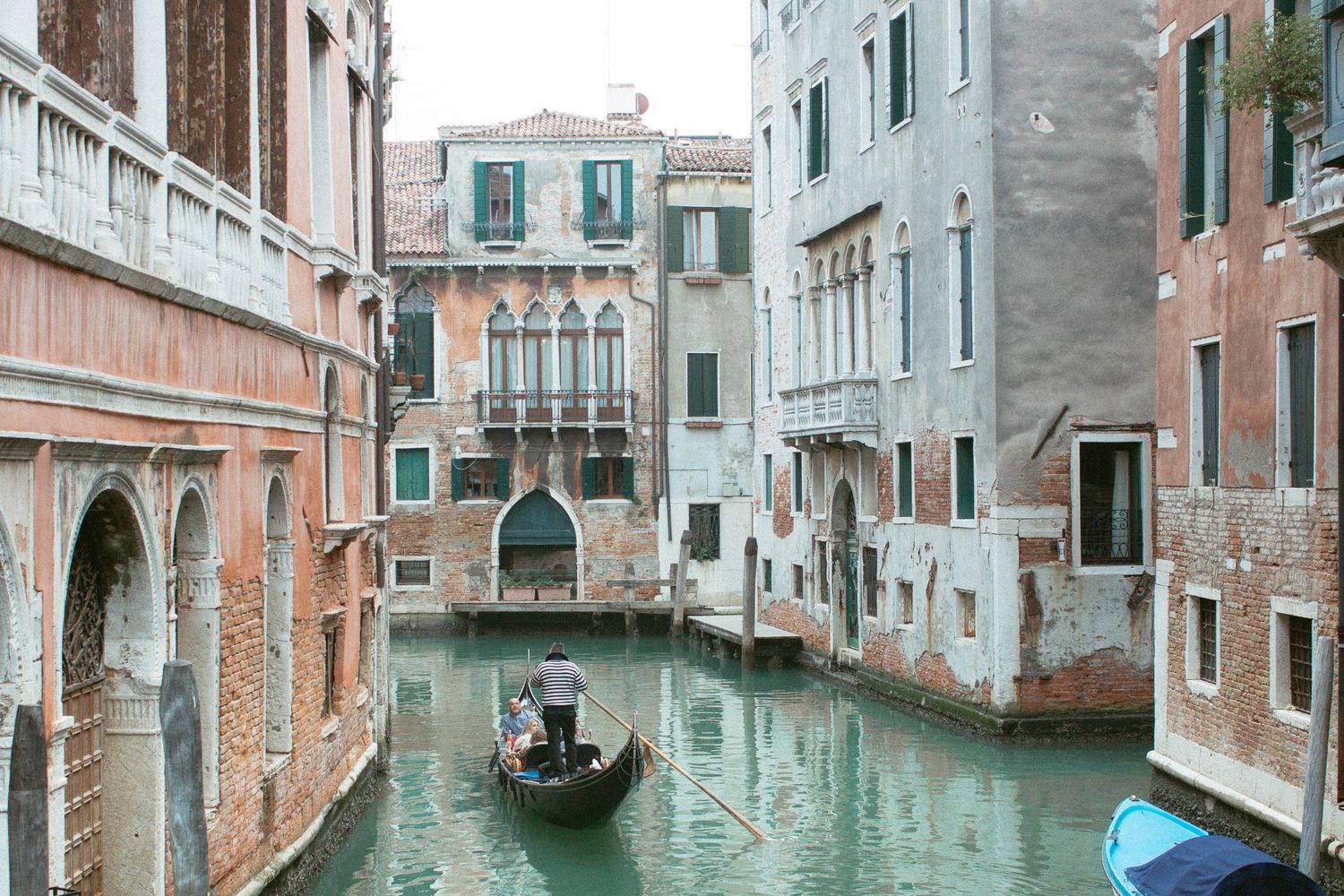 Gondolier navigating a narrow green canal between historic buildings in Venice, Italy.