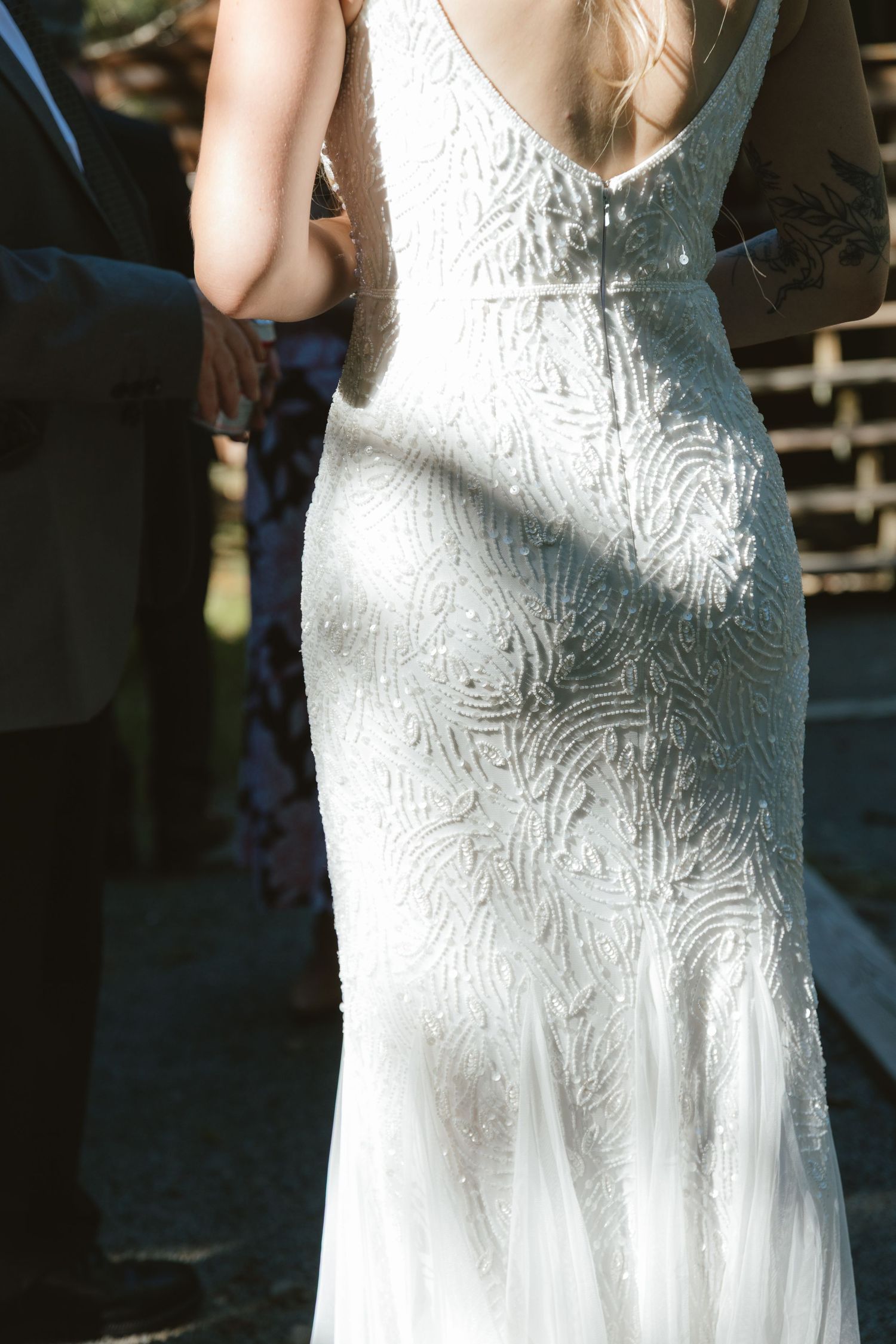 Back view of a bride in a fitted white beaded lace wedding gown with intricate swirl patterns and low back design.