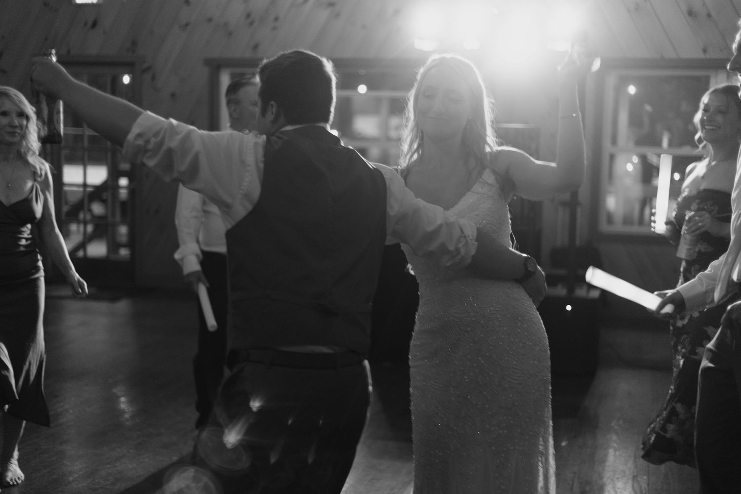 Black and white photo of a couple sharing their first dance at a wedding reception with guests watching.