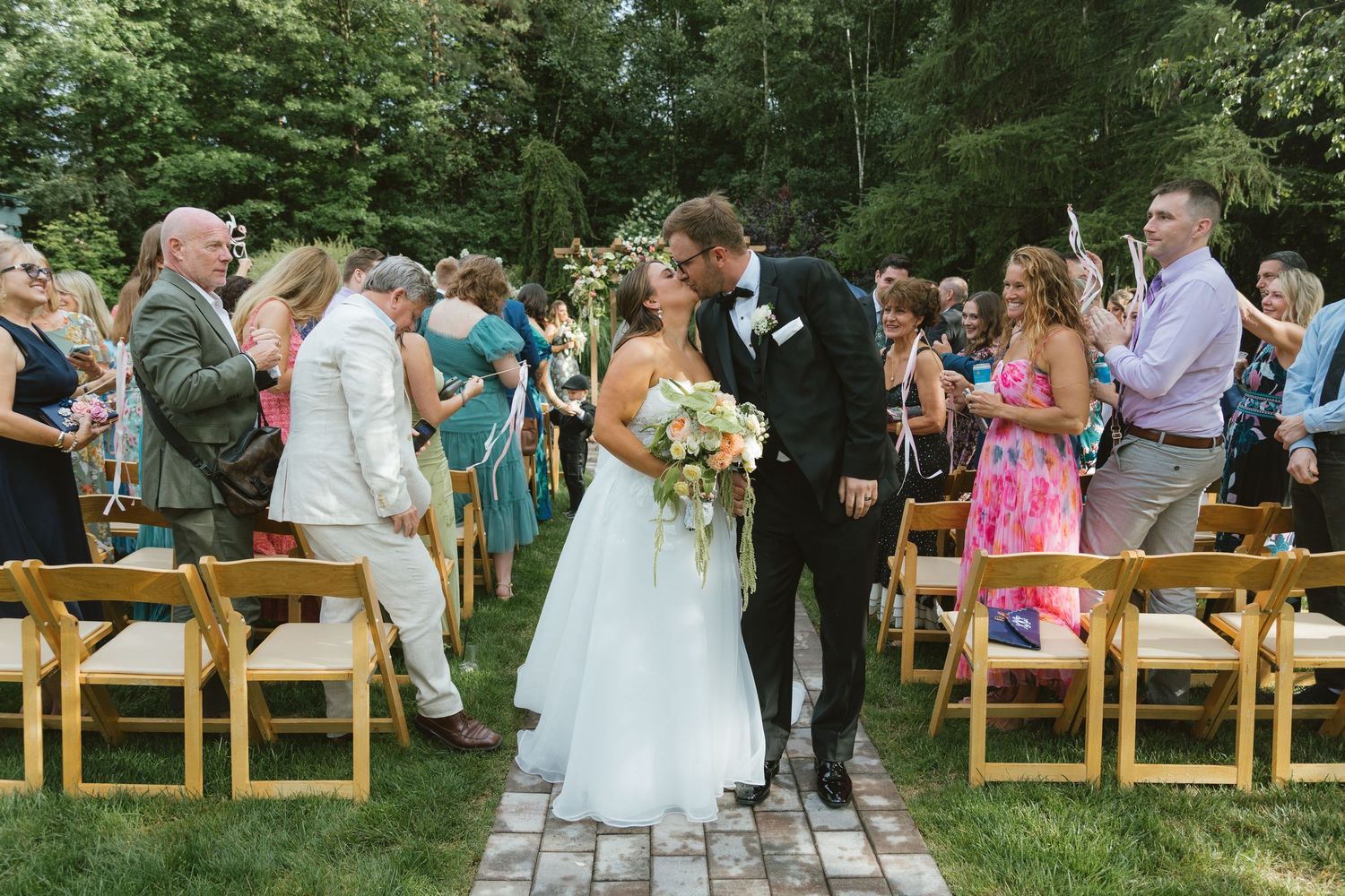 Bride and groom share a kiss while walking down the aisle at an outdoor garden wedding ceremony.