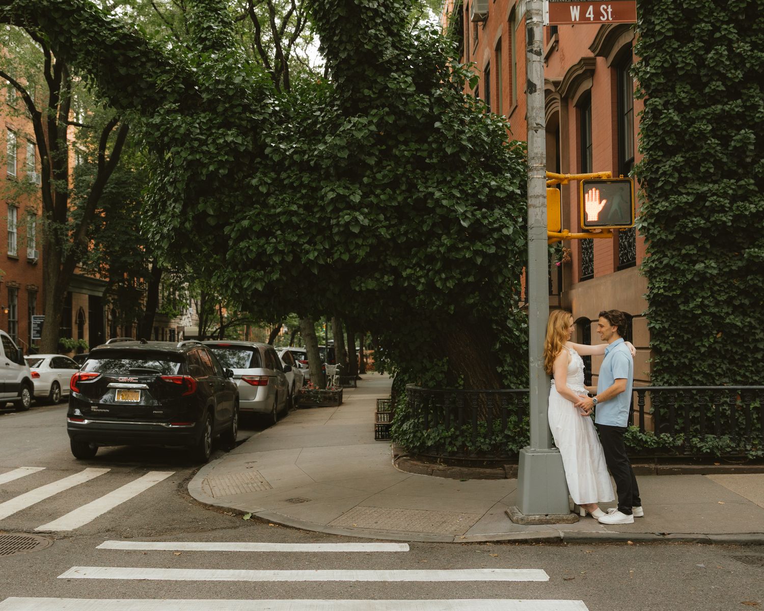 Couple sharing a romantic moment on a tree-lined NYC street corner near a crosswalk on W 4th St.
