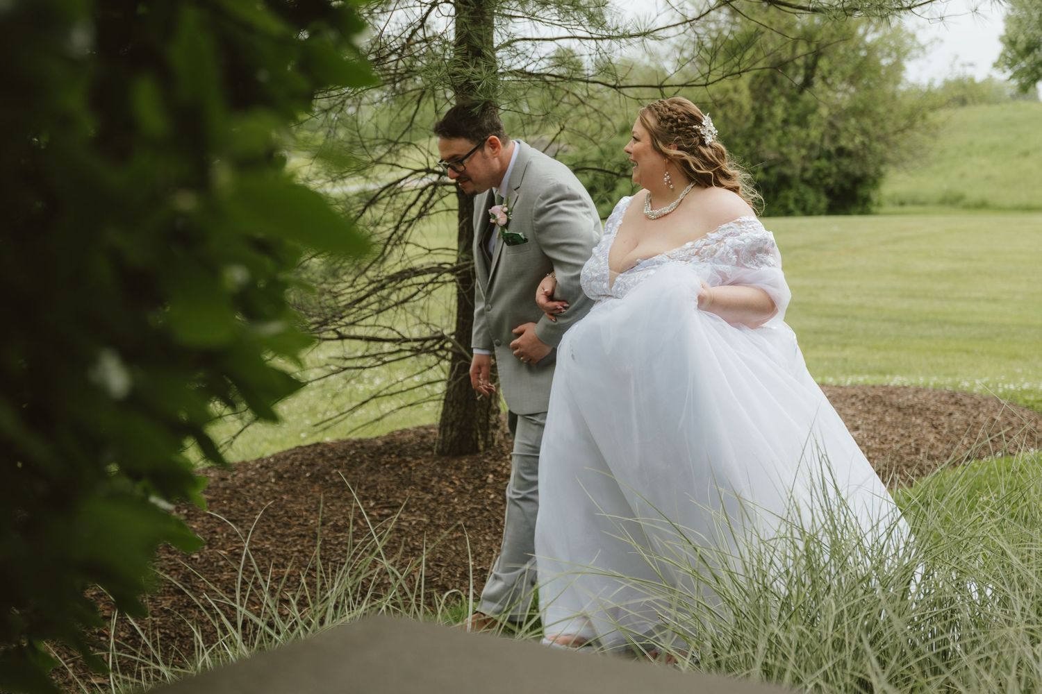 A bride in a white gown and groom in gray suit walk together outdoors on their wedding day.