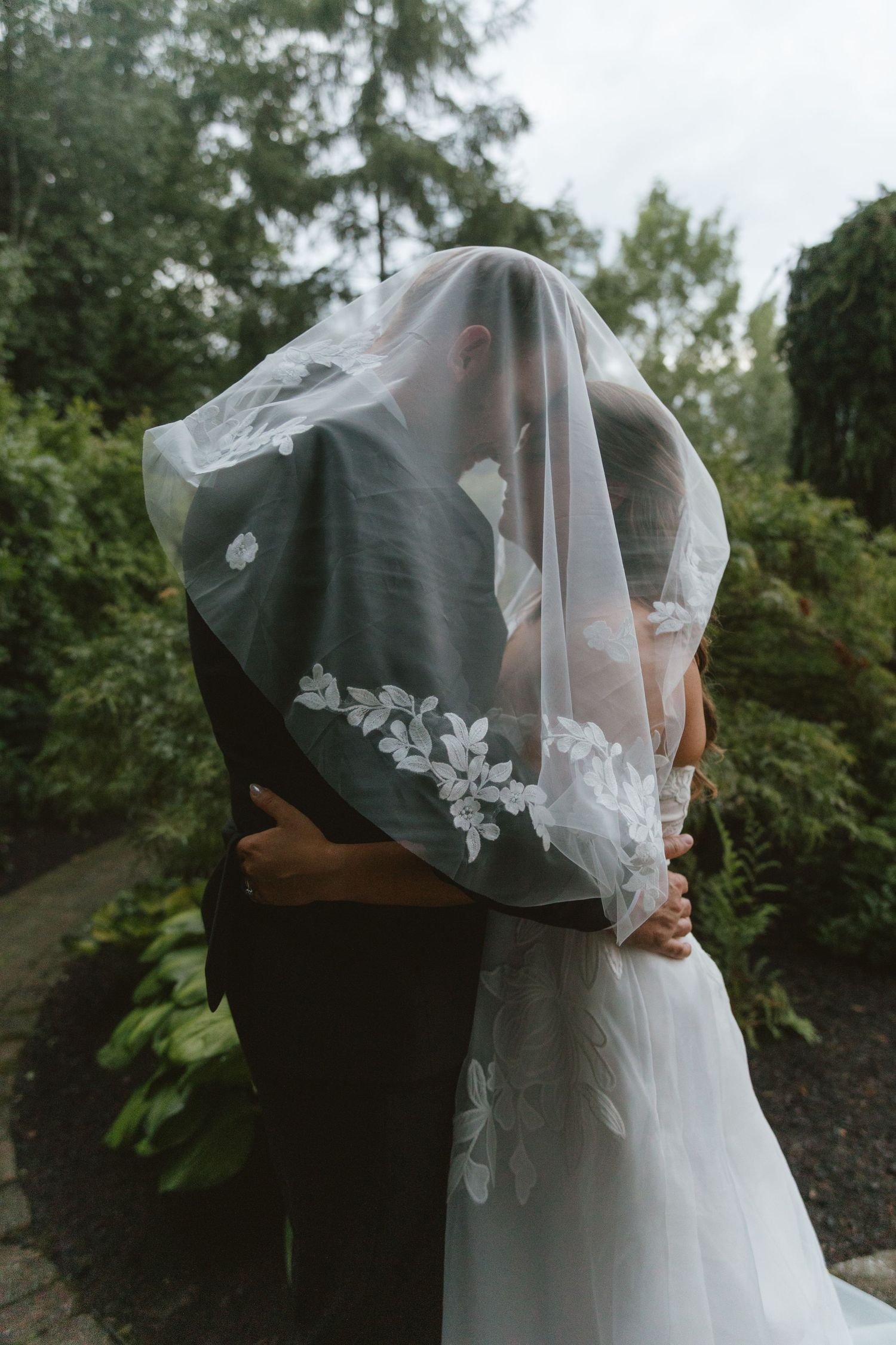 Bride and groom sharing a kiss under a lace wedding veil in a lush garden setting.