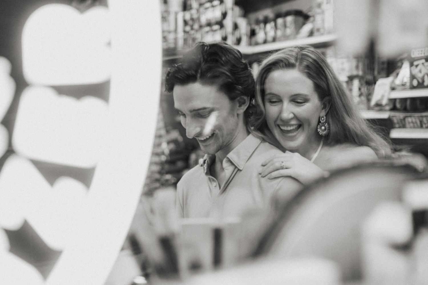 Black and white photo of a laughing couple embracing in a cozy shop, sharing a joyful moment together.