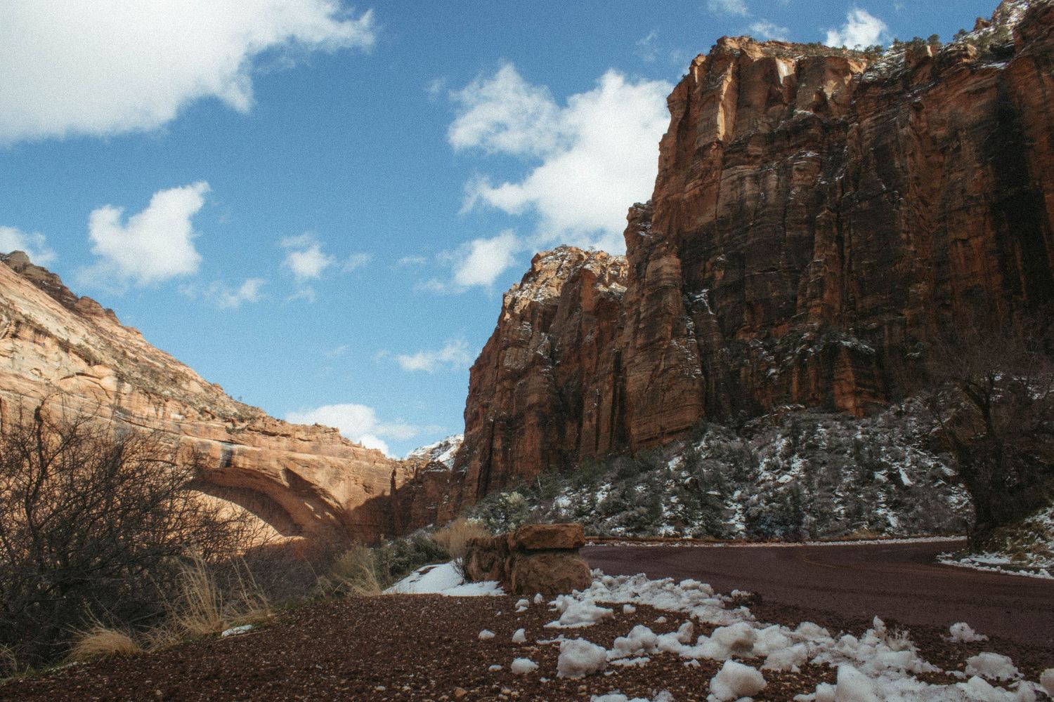 Towering red sandstone canyon walls with snow along a road in Zion National Park, Utah.