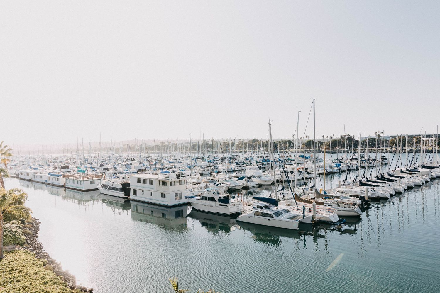 Aerial view of a busy marina filled with sailboats and yachts docked in calm harbor waters.