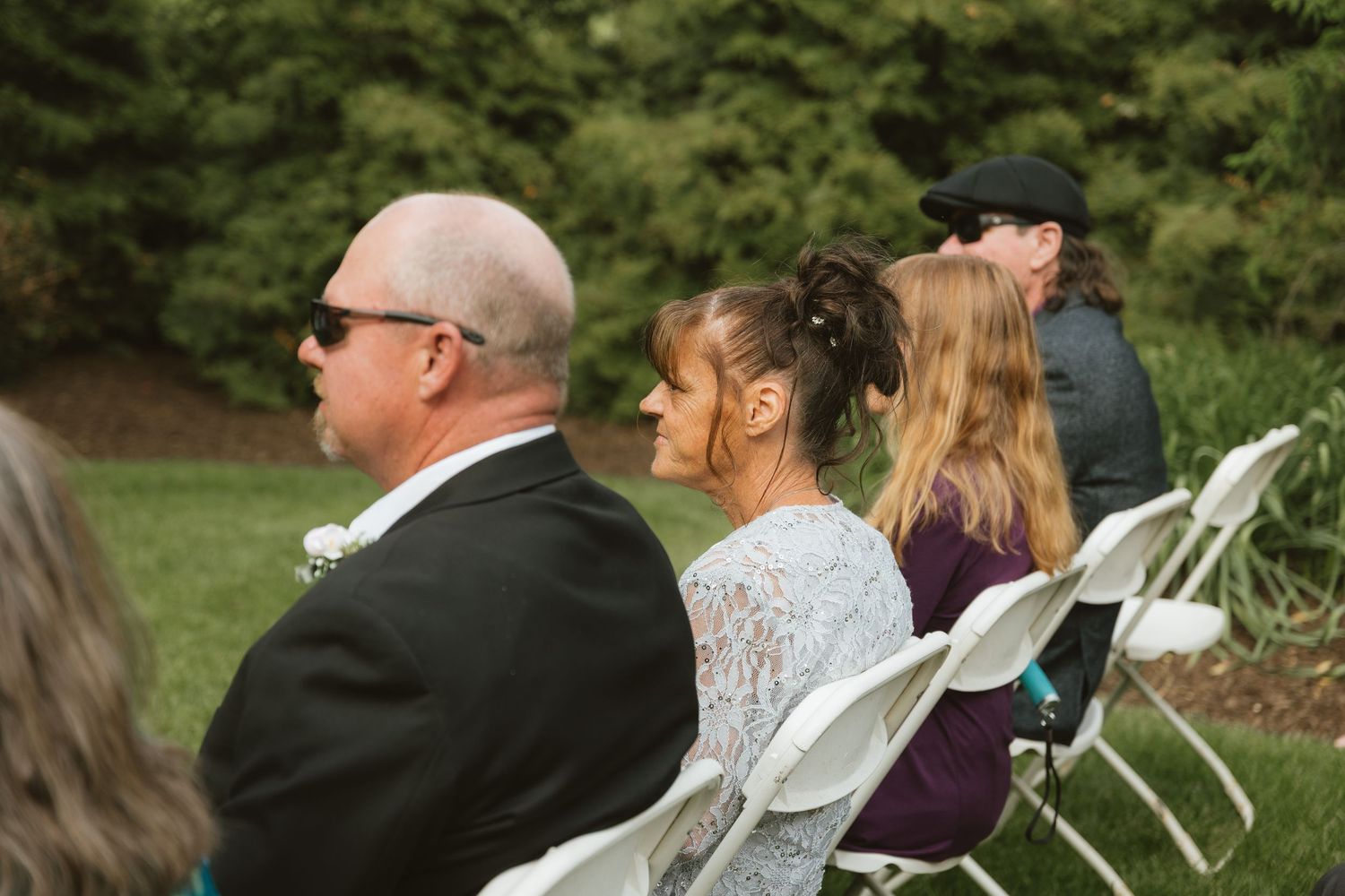 Guests seated in white chairs at an outdoor wedding ceremony on a green lawn.