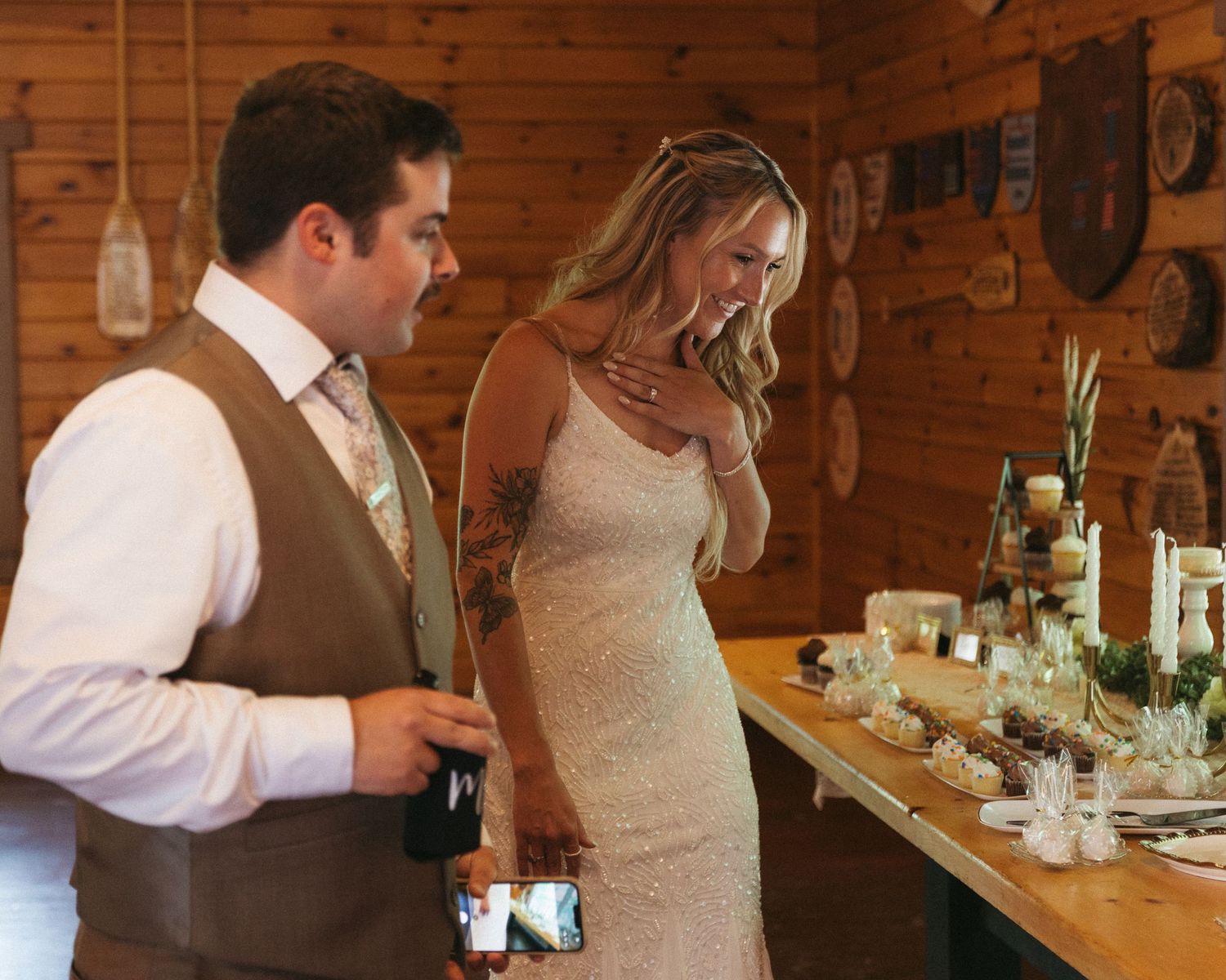 Bride and groom standing together at rustic wooden wedding venue with decorated table and candles.