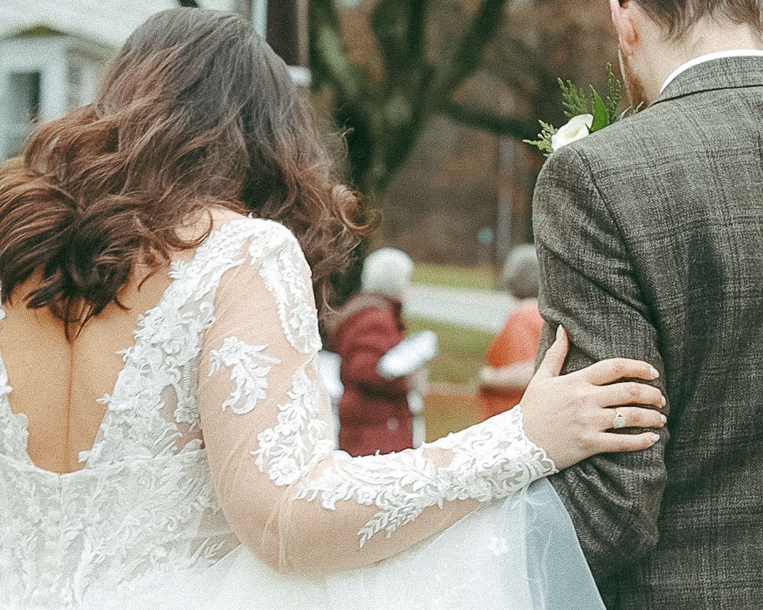 Unique shot of a bride in a lace-sleeve dress holding onto the arm of a groom in a textured suit, serving Wilkes-Barre and Scranton