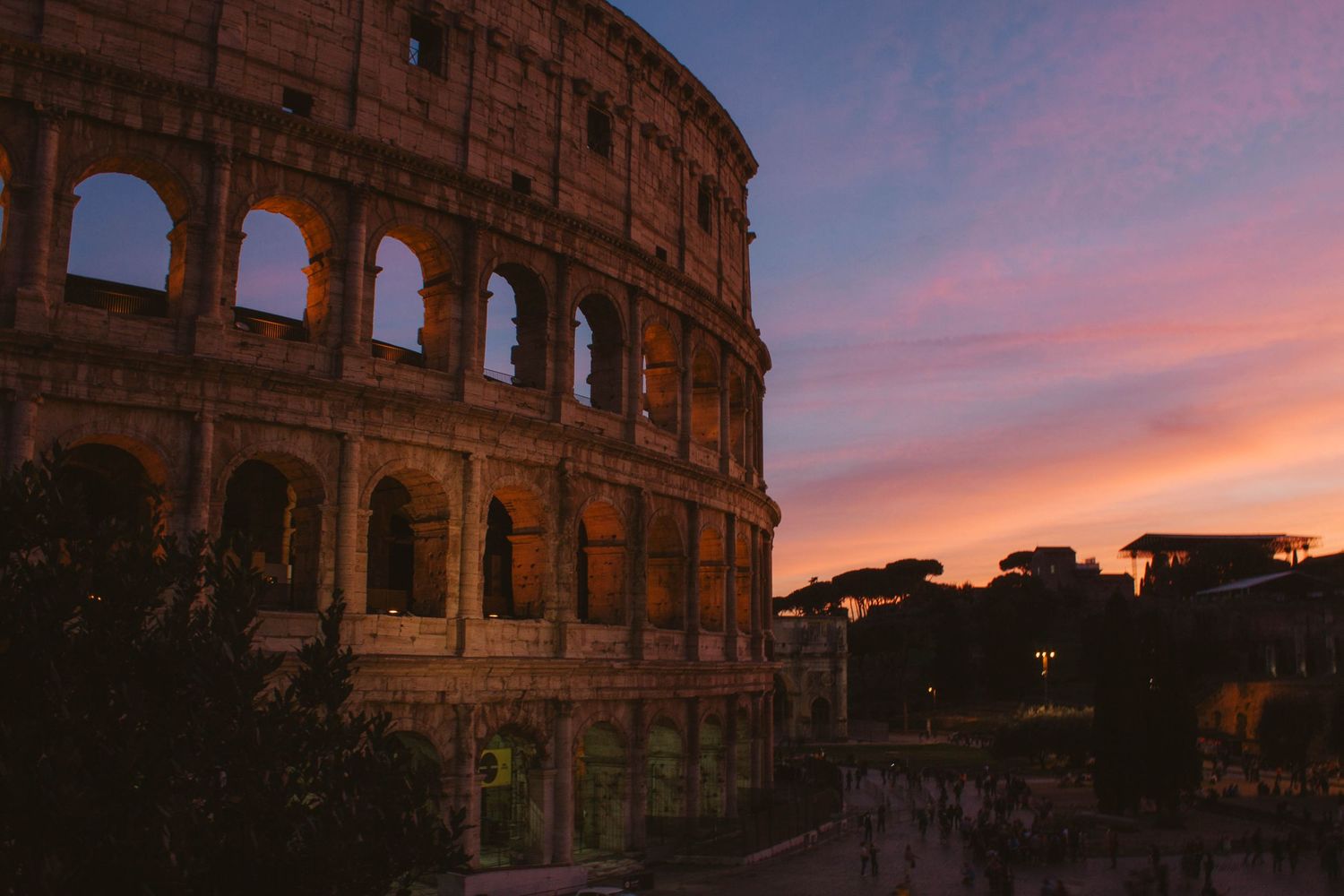The ancient Roman Colosseum illuminated against a dramatic pink and purple sunset sky in Rome.