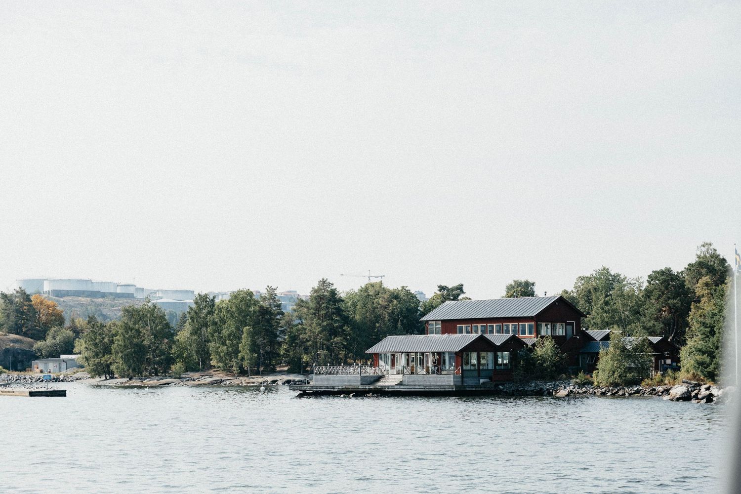 A red waterfront cabin surrounded by lush trees on a calm Swedish archipelago island.