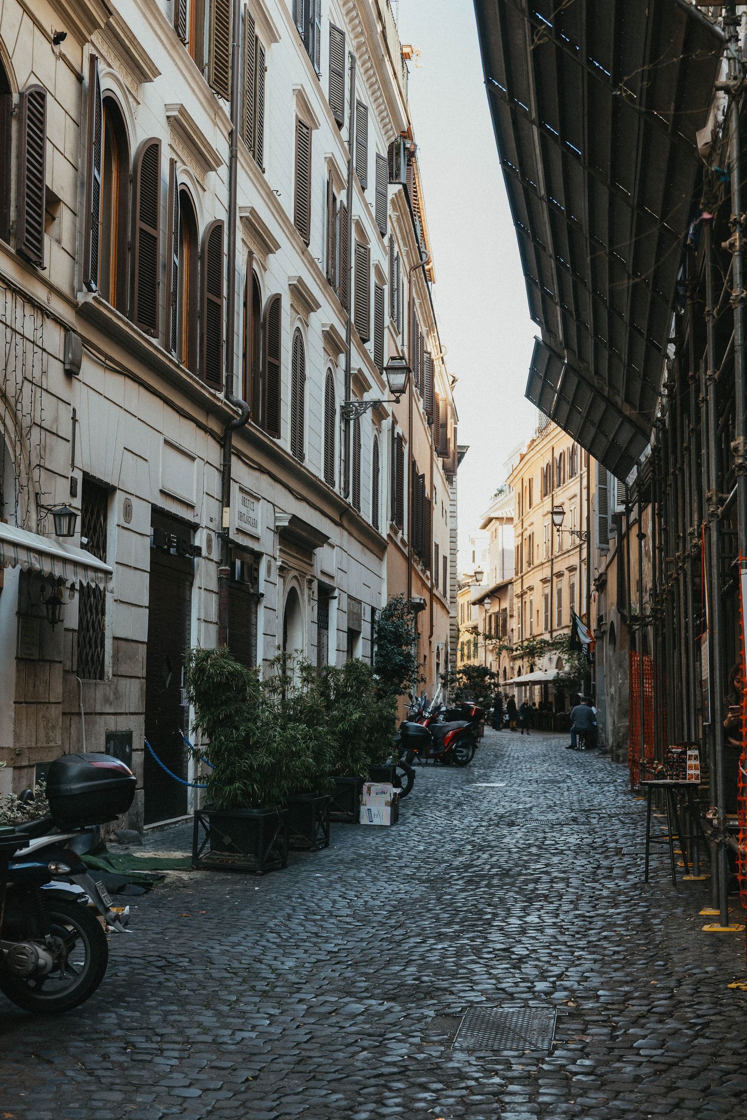 Narrow cobblestone street lined with historic buildings and parked scooters in Rome, Italy.
