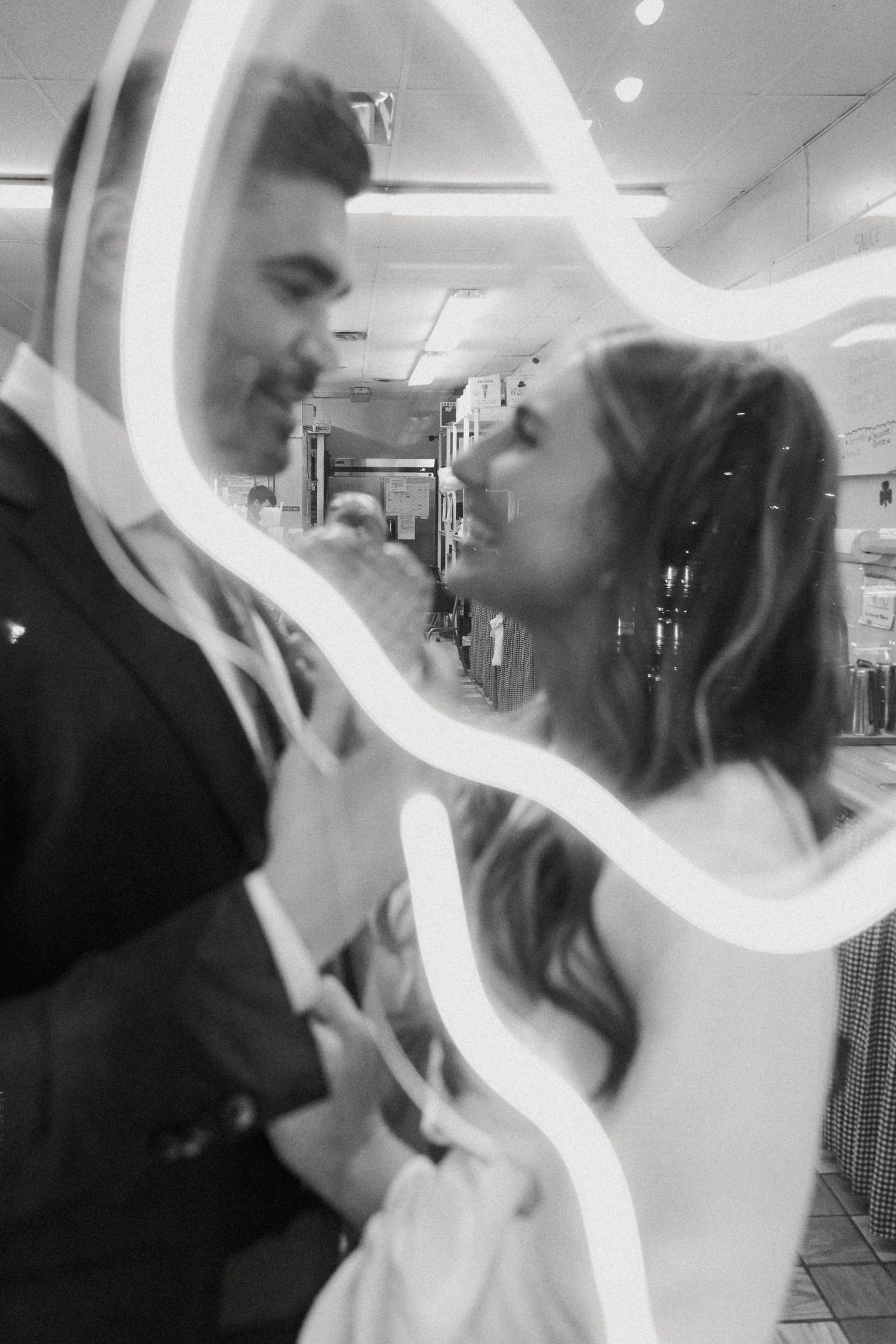 Black and white artistic photo of bride and groom framed by glowing neon light at reception.