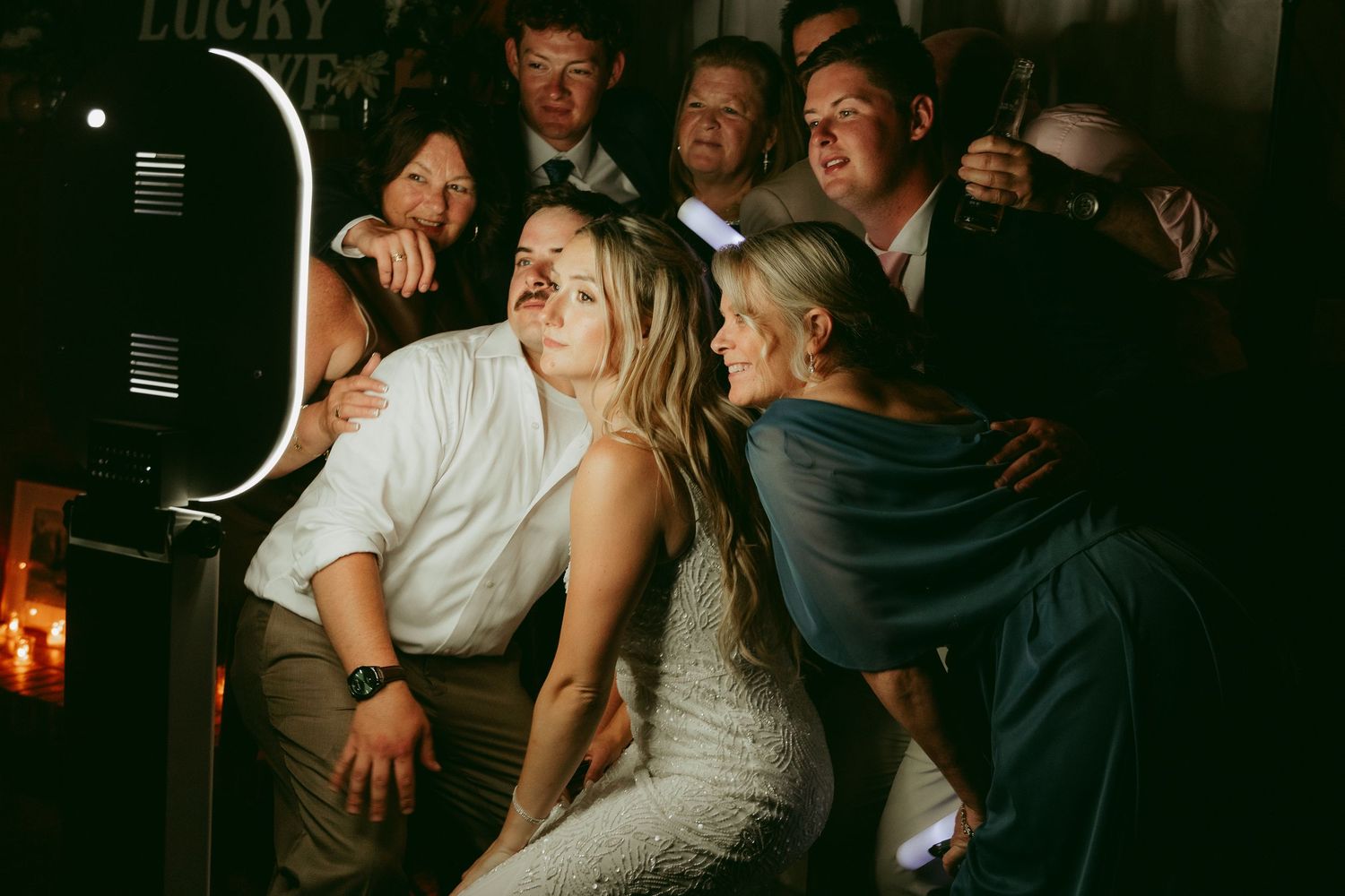 Group of wedding guests crowding around a photo booth, smiling and posing together at a reception.