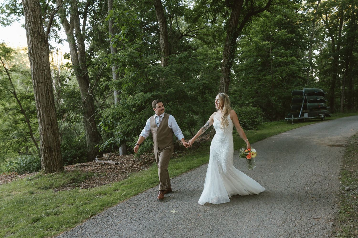 Bride and groom holding hands walking down a tree-lined path on their wedding day.