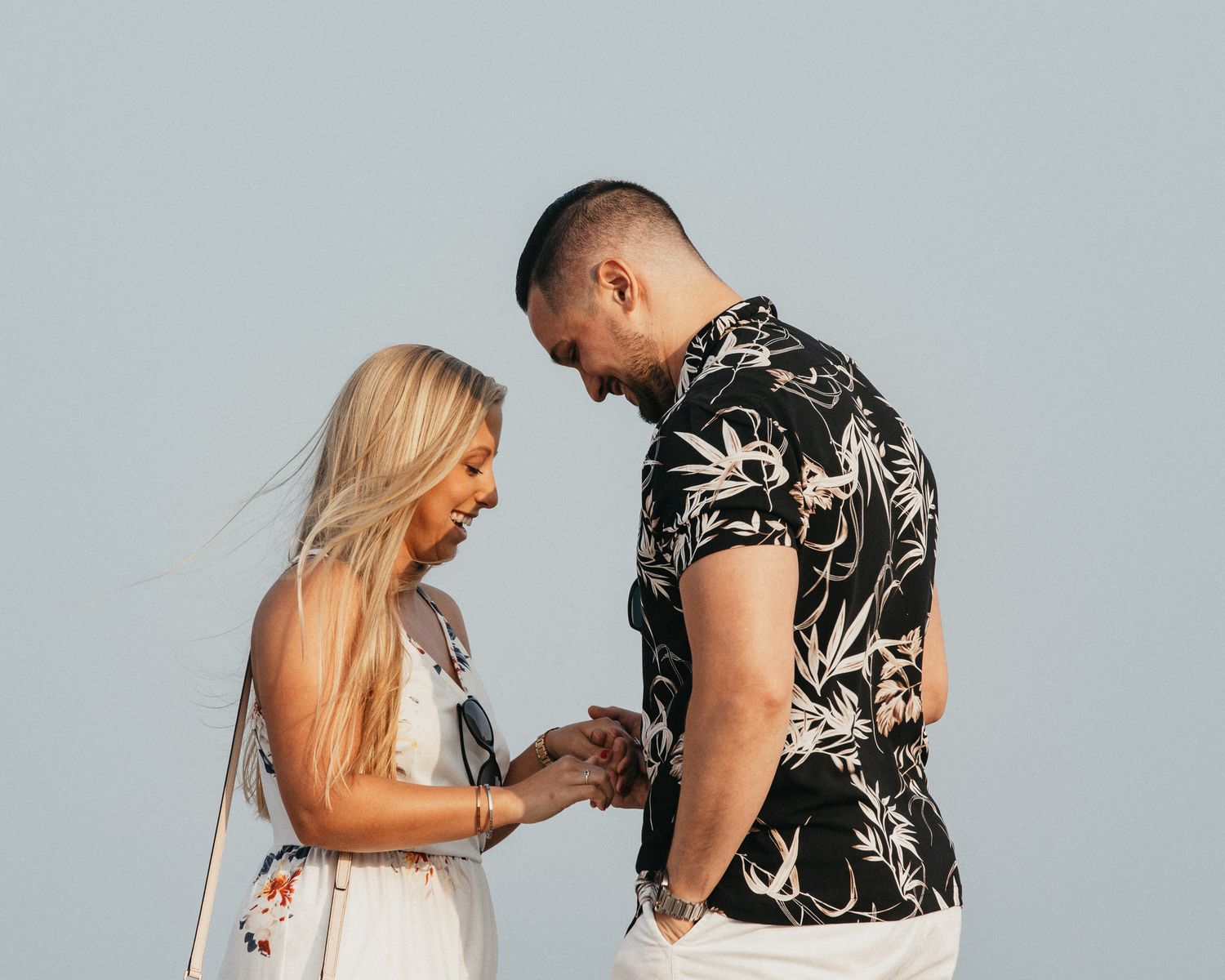 Couple sharing intimate moment as man places engagement ring on womans finger outdoors.