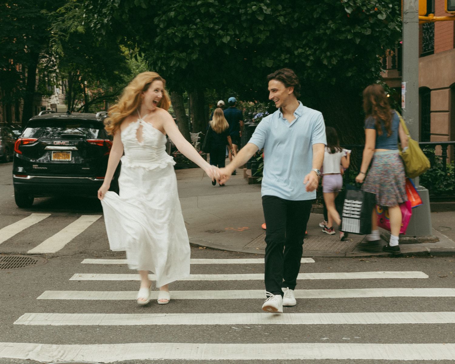 Couple holding hands crossing a zebra crossing in New York City, woman in white dress, man in blue shirt.