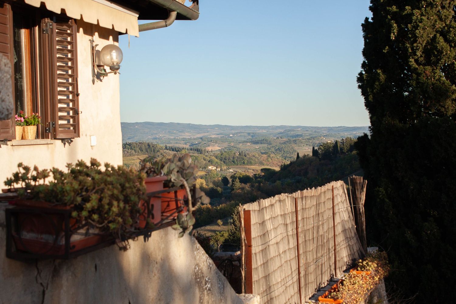 A rustic Tuscan hillside villa with terracotta pots and rolling green valley views at golden hour.