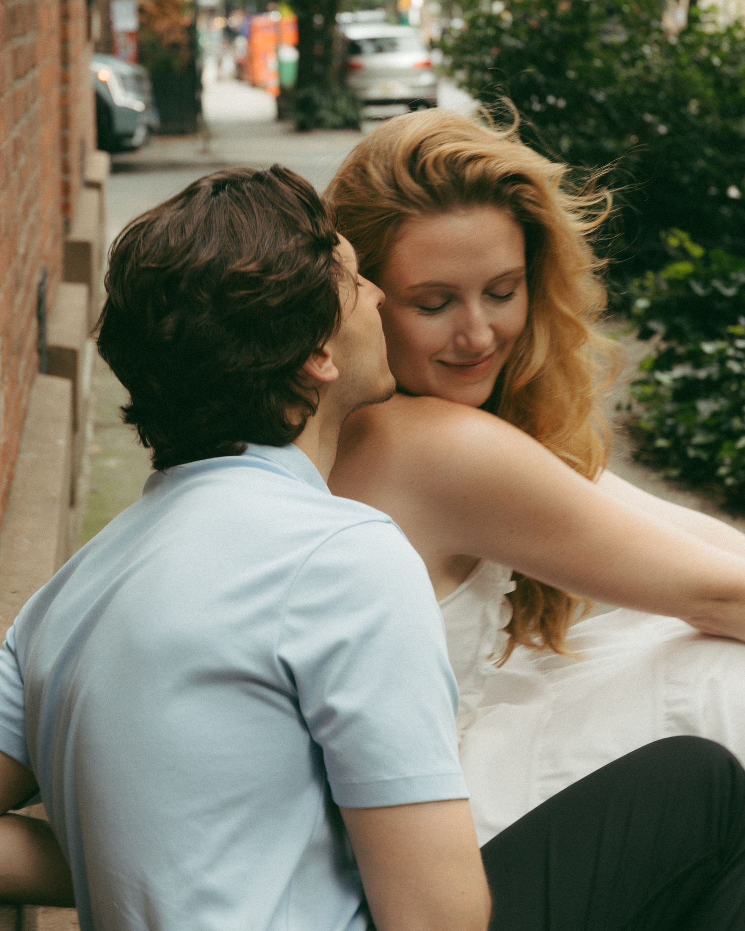 Young couple sharing a tender moment outdoors, woman smiling as man leans in close on a city street.