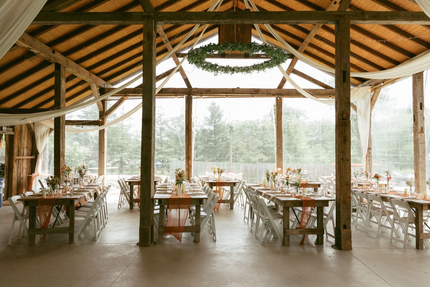 Rustic barn wedding reception venue with long wooden tables and greenery chandelier decor.
