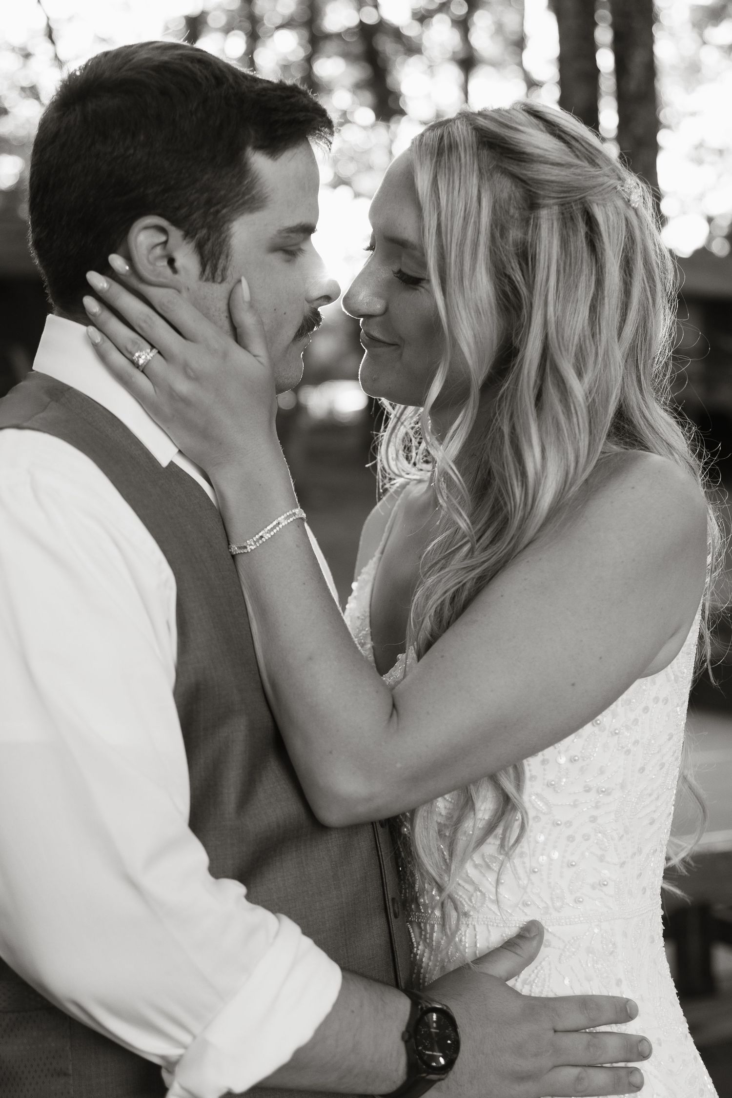 Black and white wedding photo of bride and groom sharing a romantic almost-kiss, bride tenderly holding groom's face.