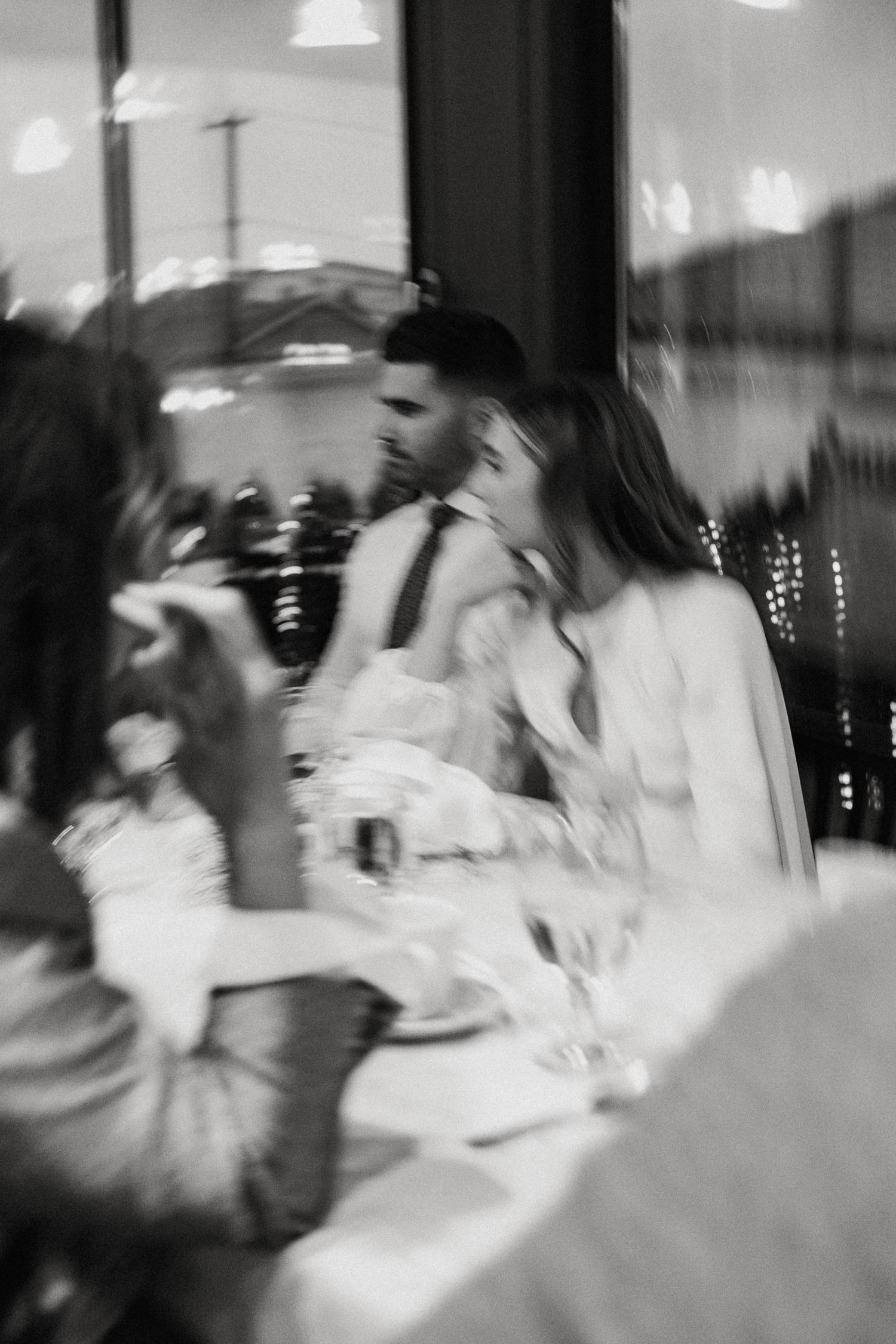 Blurred black and white photo of bride and groom sharing a kiss at wedding reception table.