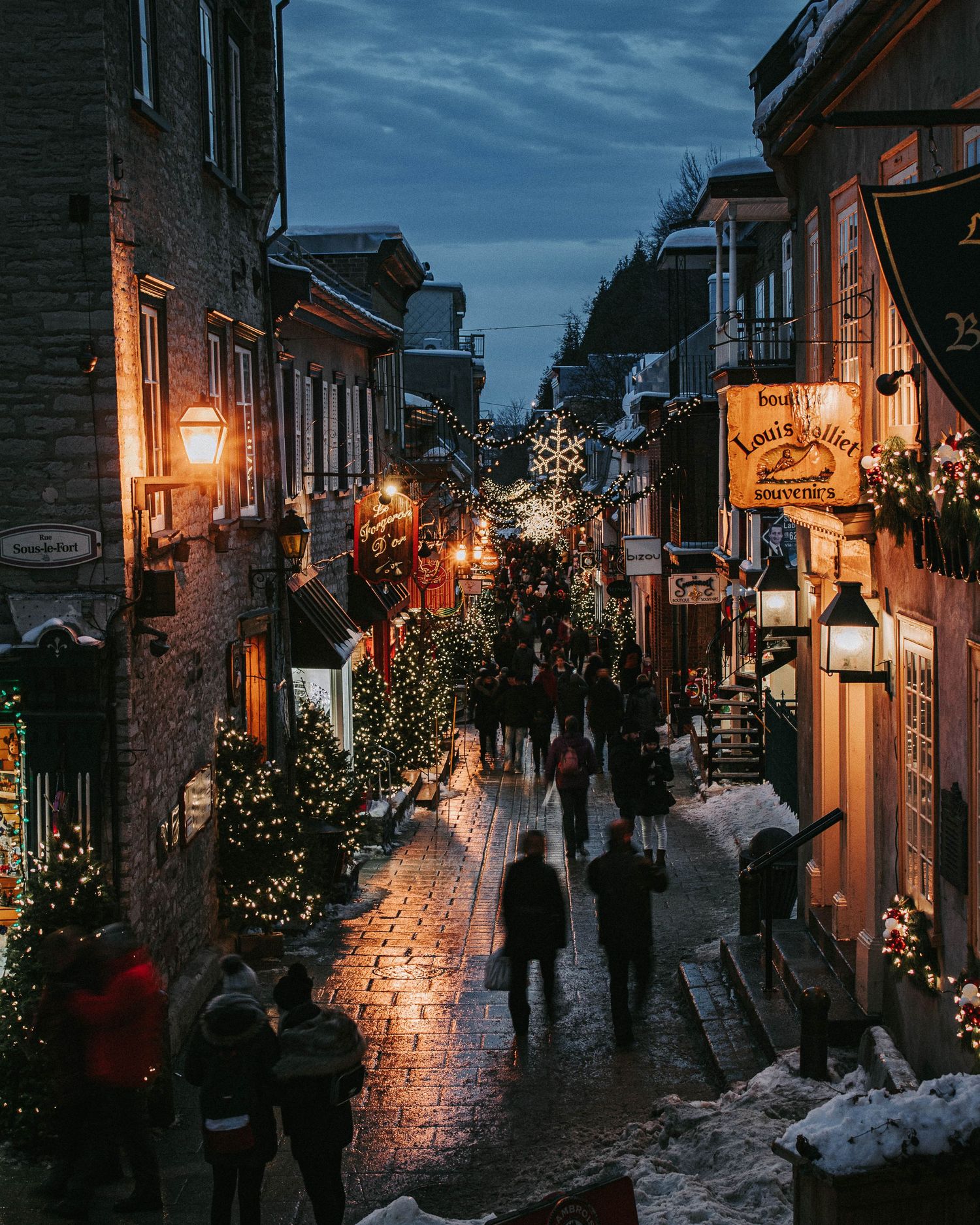 Charming Christmas-lit cobblestone street in Old Quebec City glowing at dusk in winter.