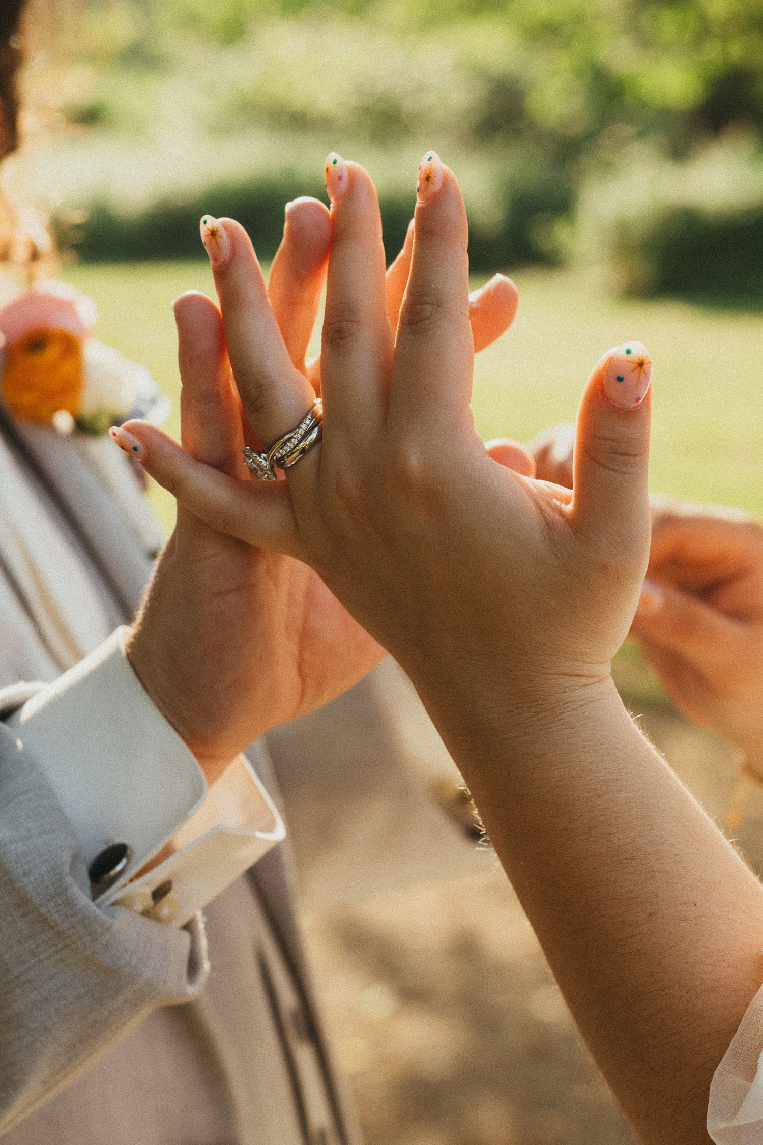Close-up of bride and groom hands showing wedding rings with decorative nail art at outdoor ceremony.