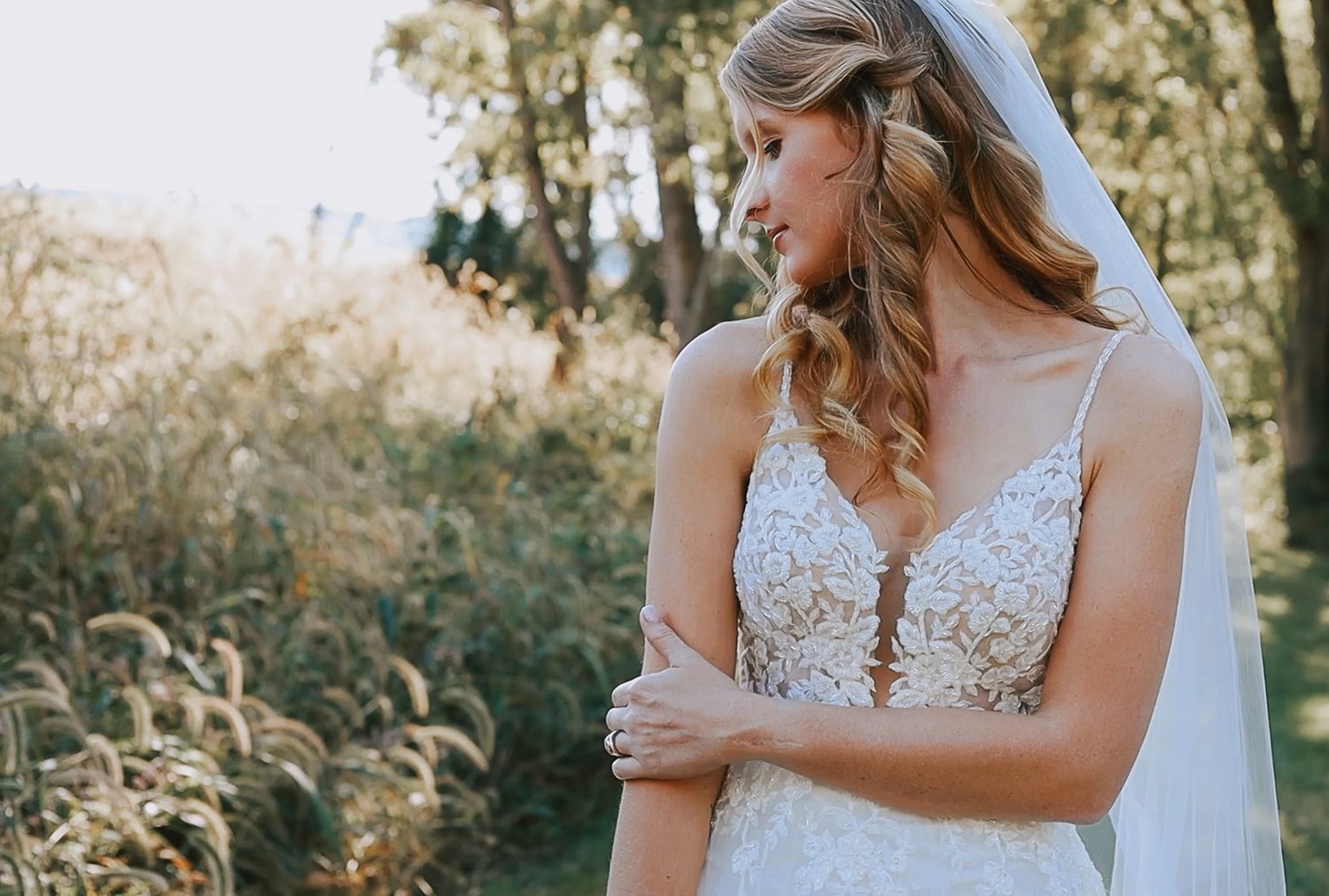 Bride in lace spaghetti strap wedding gown with veil standing in golden field.