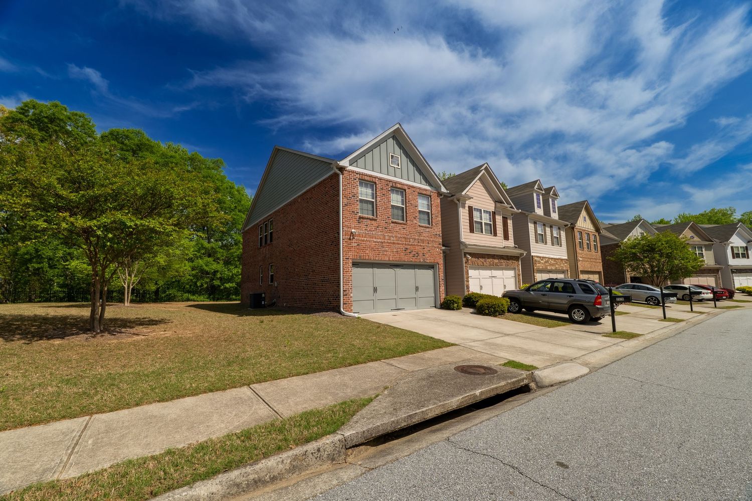 A panoramic view of a residential neighborhood with brick houses and driveways under a vibrant blue sky with white clouds.