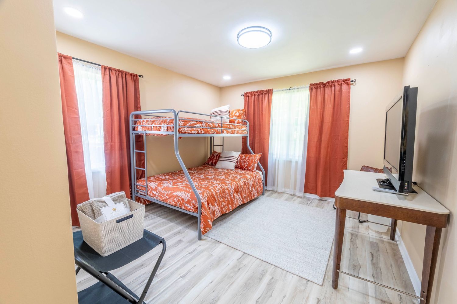 Modern bedroom interior with orange curtains, flat-screen TV, and beige walls shown from multiple angles.