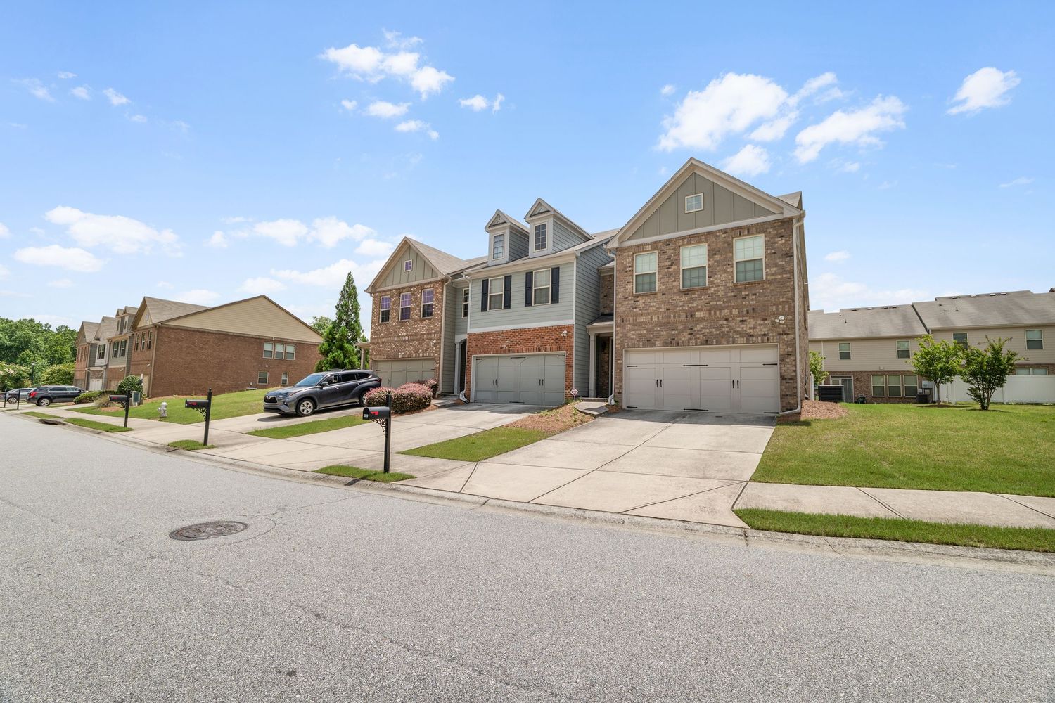Panoramic view of suburban houses with well-maintained lawns and driveways along a quiet residential street.