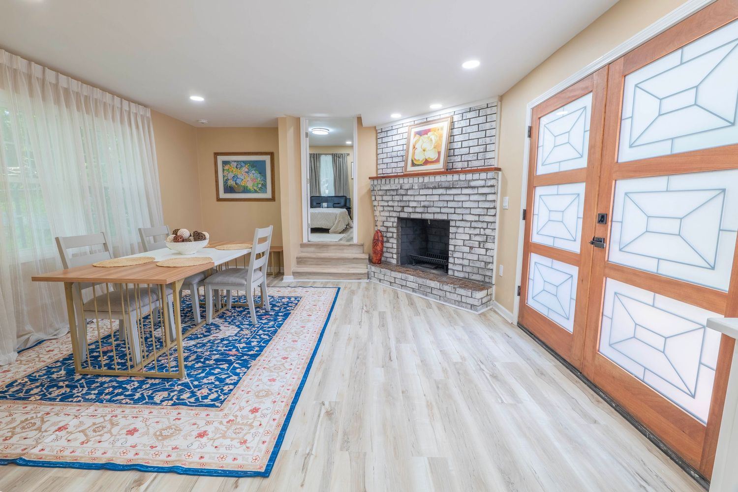 Modern living room with corner brick fireplace, light wood floors, blue area rug, and decorative glass panel doors.