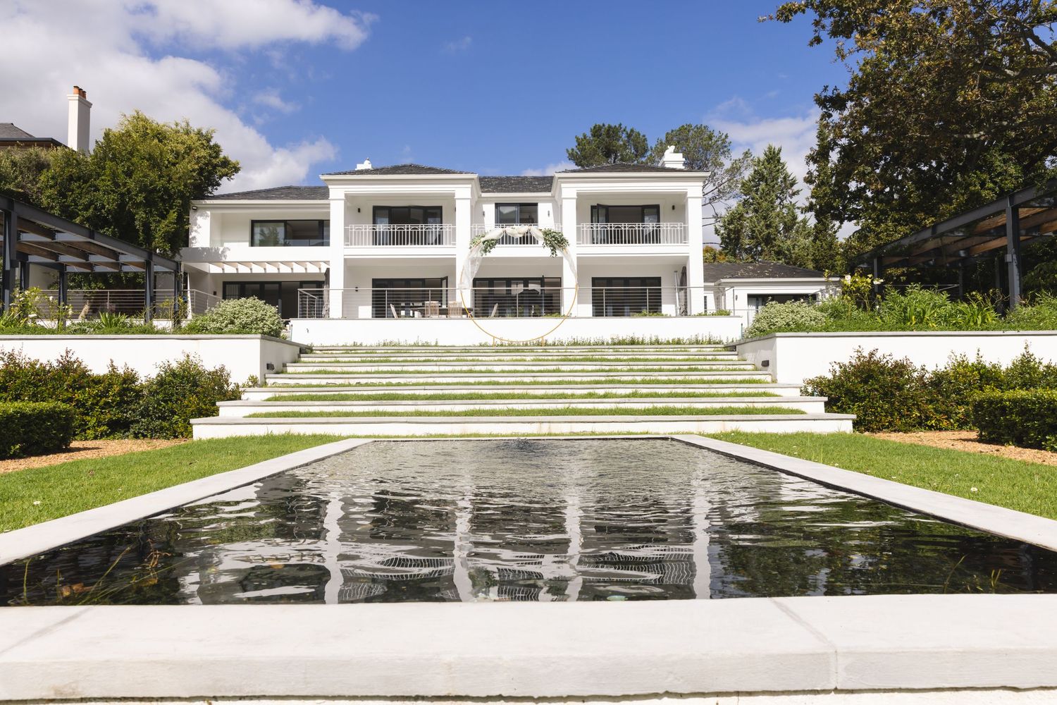 A modern white villa with reflecting pools and terraced levels creates a stunning architectural composition against blue skies.