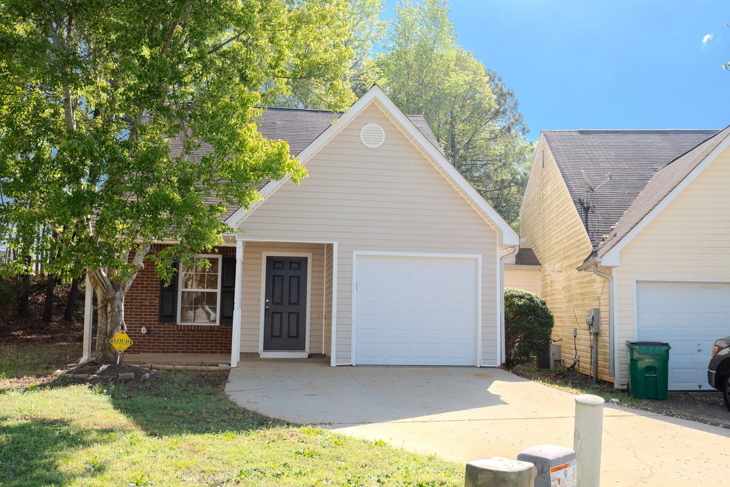 White residential garage door with tan siding and landscaping visible in a suburban neighborhood setting.