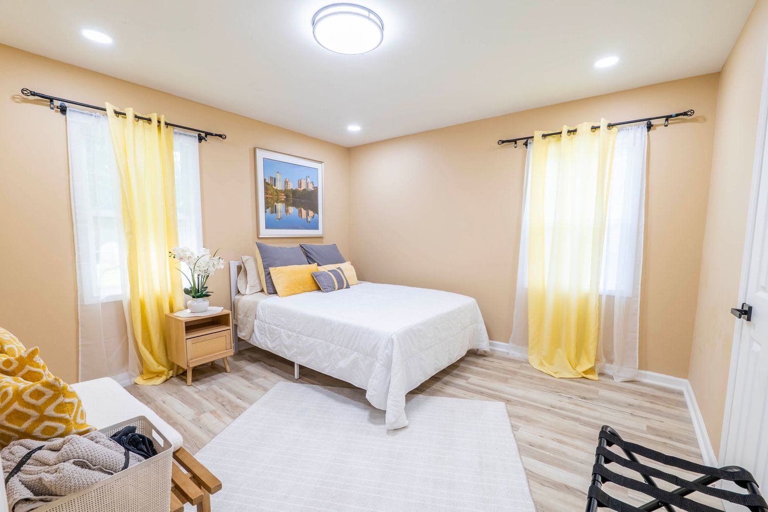 Bright modern bedroom with yellow curtains, white walls, recessed lighting and hardwood floors.